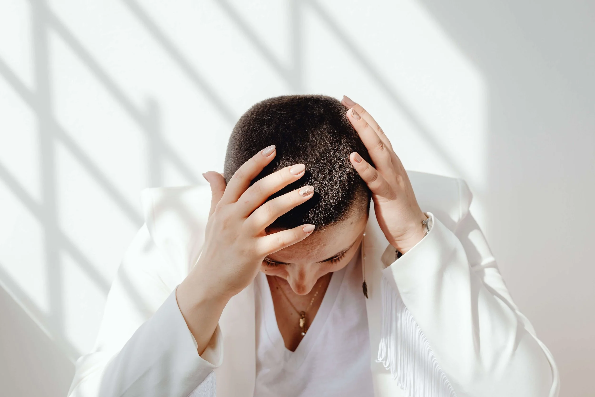 Person with a shaved head looking down and holding their head in their hands, representing emotional distress explored with a trauma therapist for young adults in Manhattan.