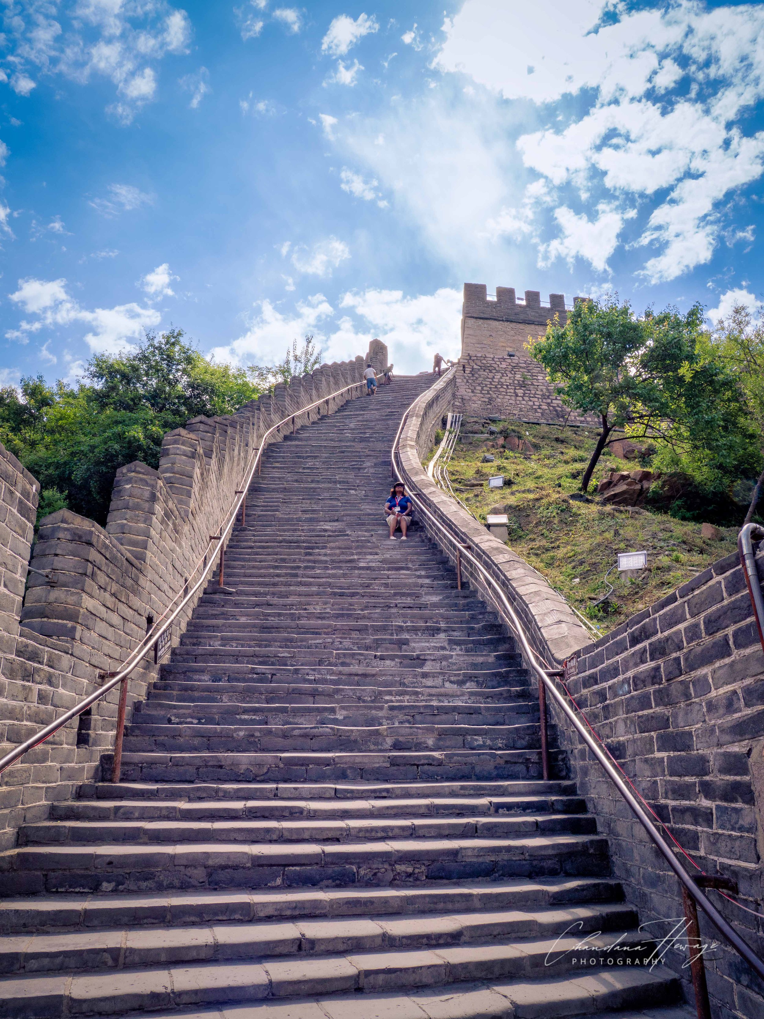 Nali is resting before climbing further.
On the right, a high stone platform wall topped with traditional defensive crenels. This structural design allowed guards on the upper level to defend the vulnerable staircase below.