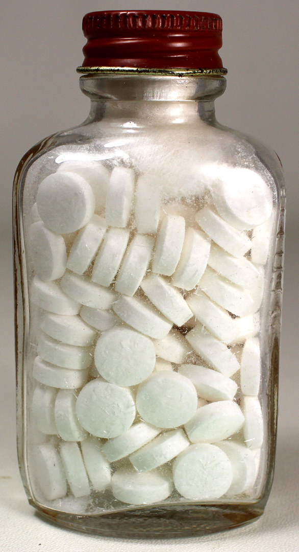 A glass jar filled with white pills and tablets with a red metal screw-on lid.