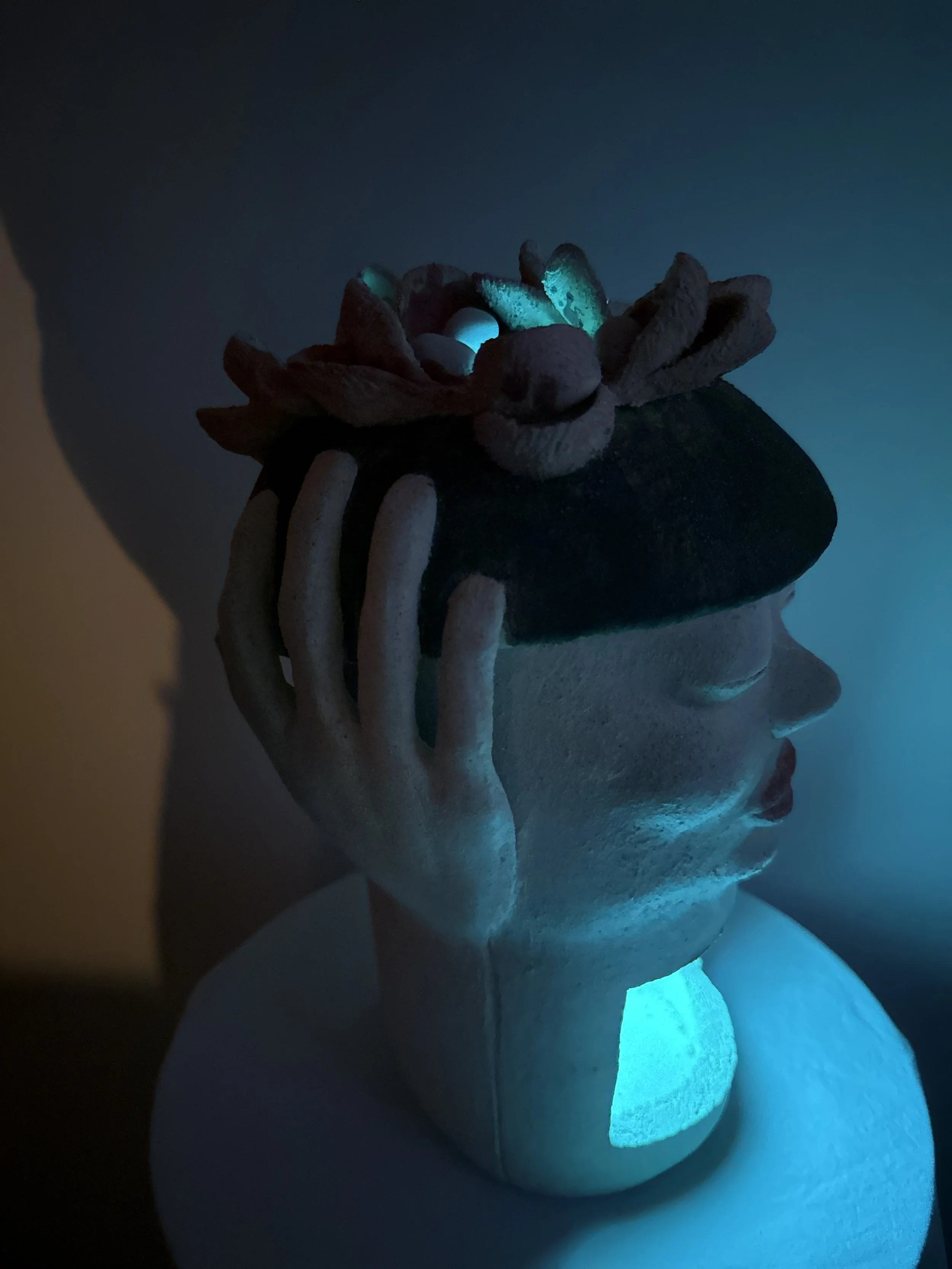 An stoneware ceramic sculpture portrait titled ‘Beret Adjustment’ bathed in soft teal color from a LED light in it’s interior.
