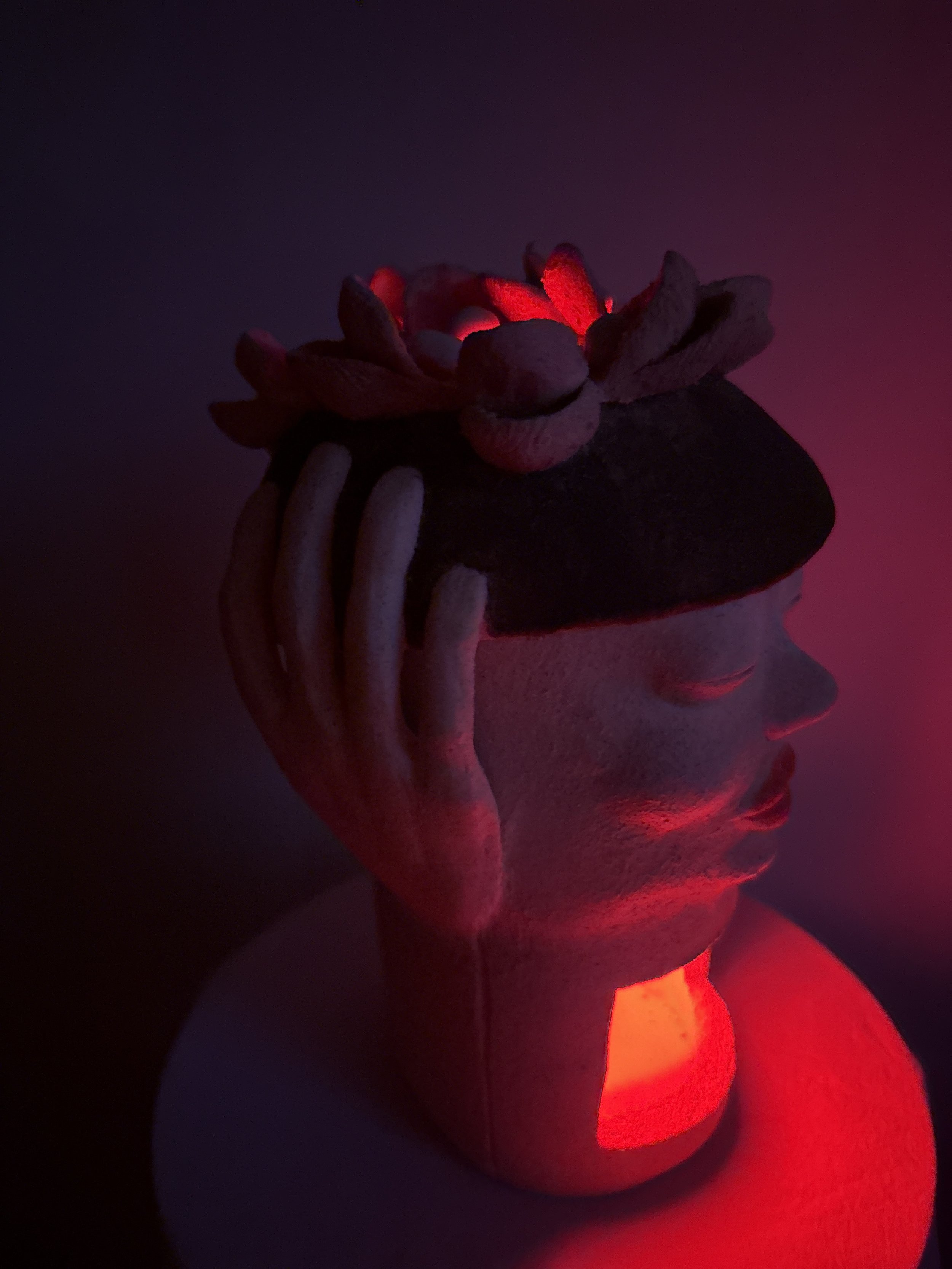 An stoneware ceramic sculpture portrait titled ‘Beret Adjustment’ bathed in soft red color from a LED light in it’s interior.