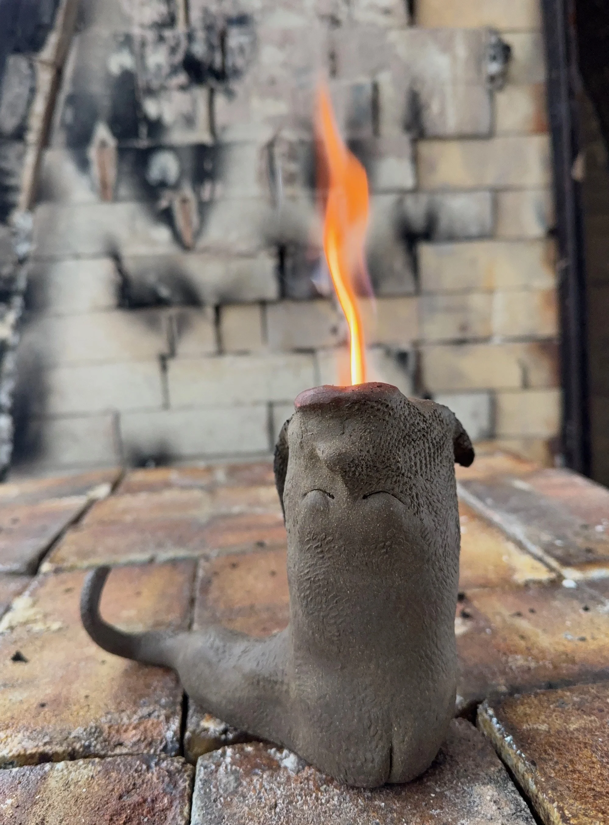 A serpent like dark brown clay ceramic sculpture with fire coming out the top.