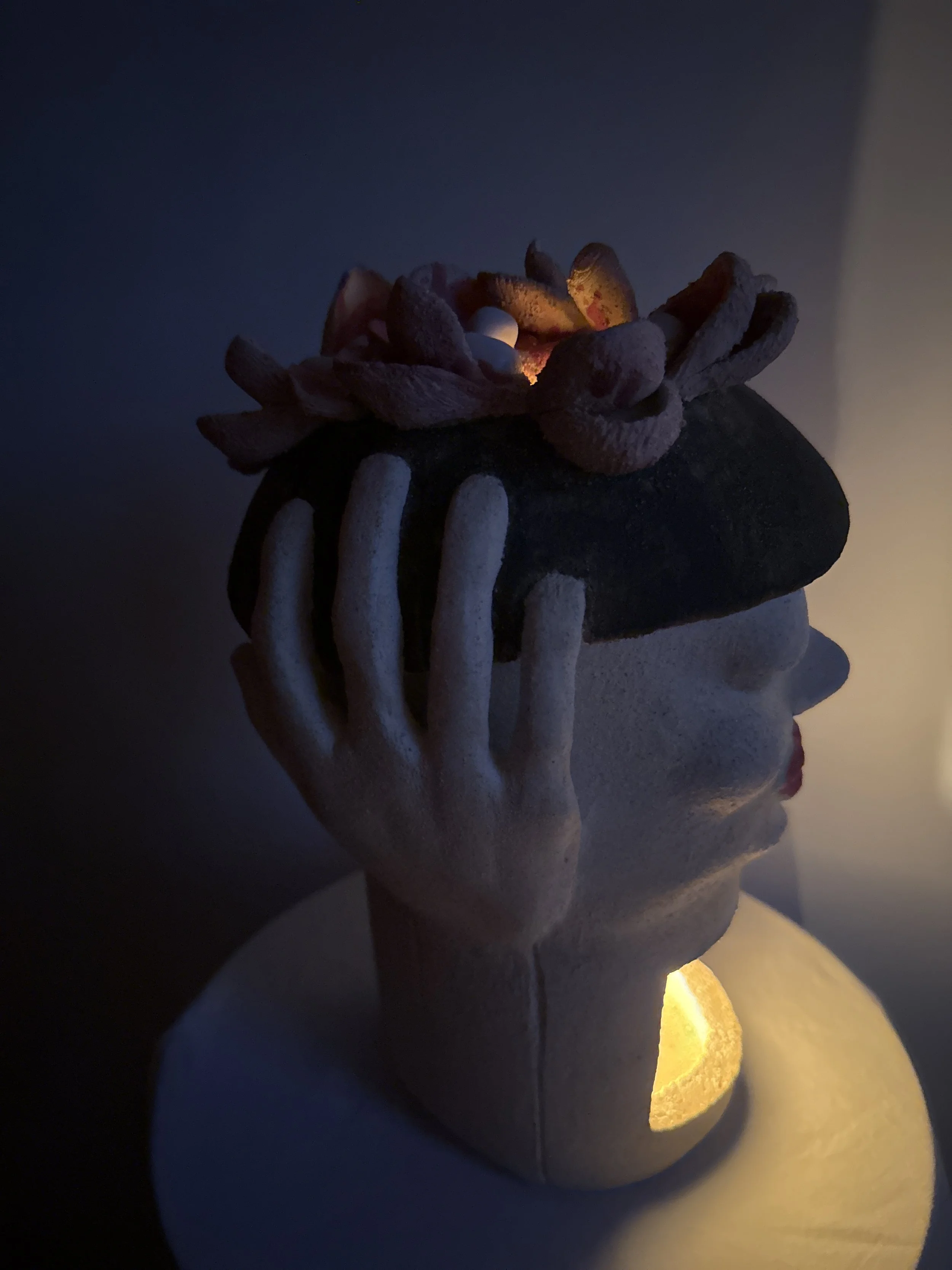 An stoneware ceramic sculpture portrait titled ‘Beret Adjustment’ bathed in soft warm white color from a LED light in it’s interior.