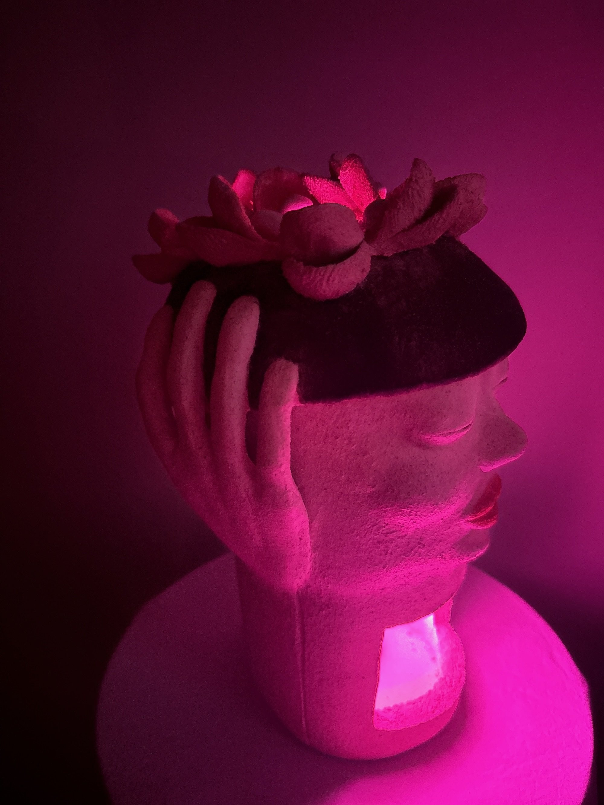 A white stoneware ceramic sculpture titled ‘Beret Adjustment’, featuring full red lips, a black beret with pink flowers on top, and a pink LED light in the base