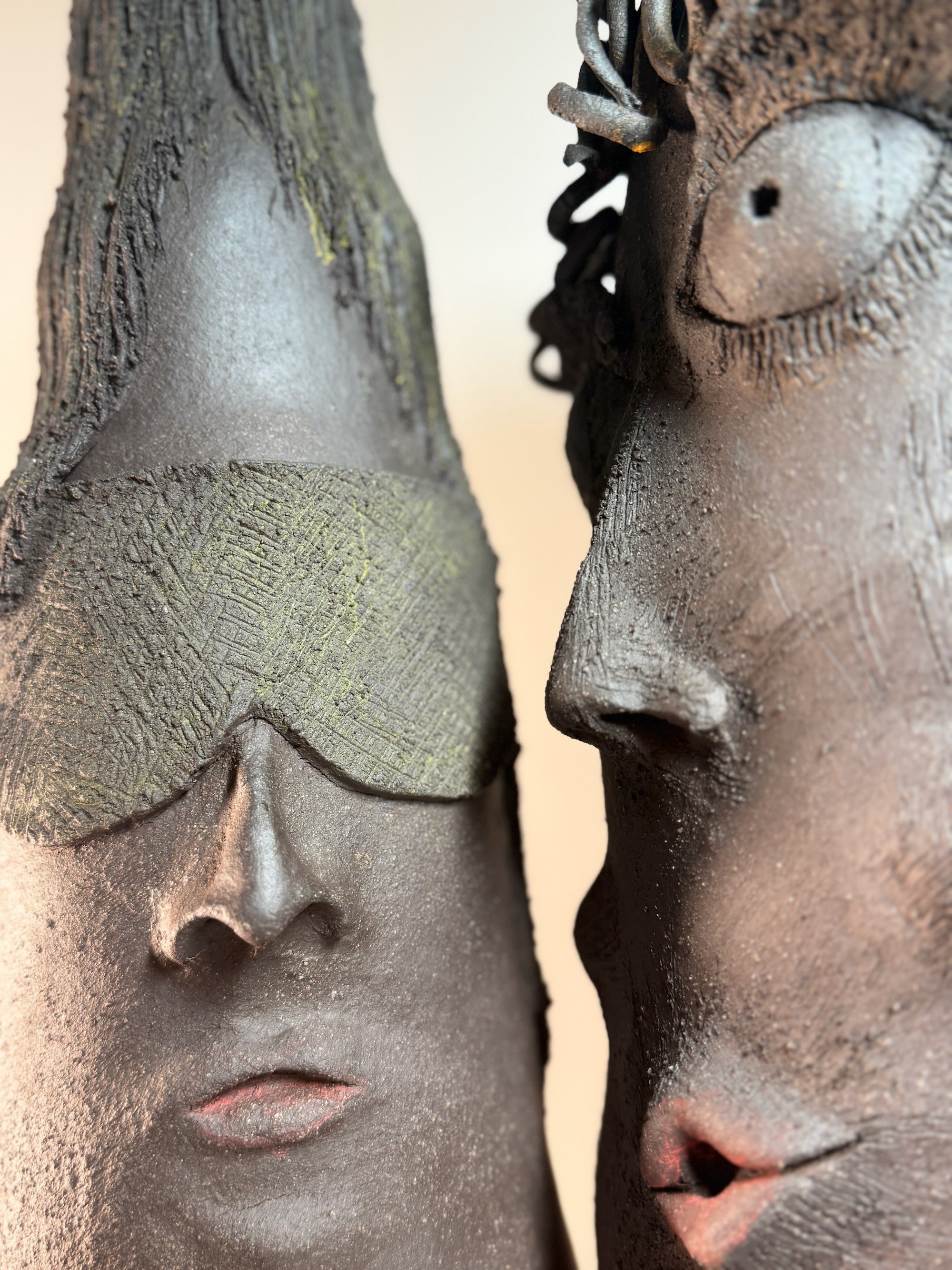 Detail of two dark black stoneware ceramic sculptures titled 'Dude and Dudette', featuring expressive chiseled facial features and hand-coiled hair curls.