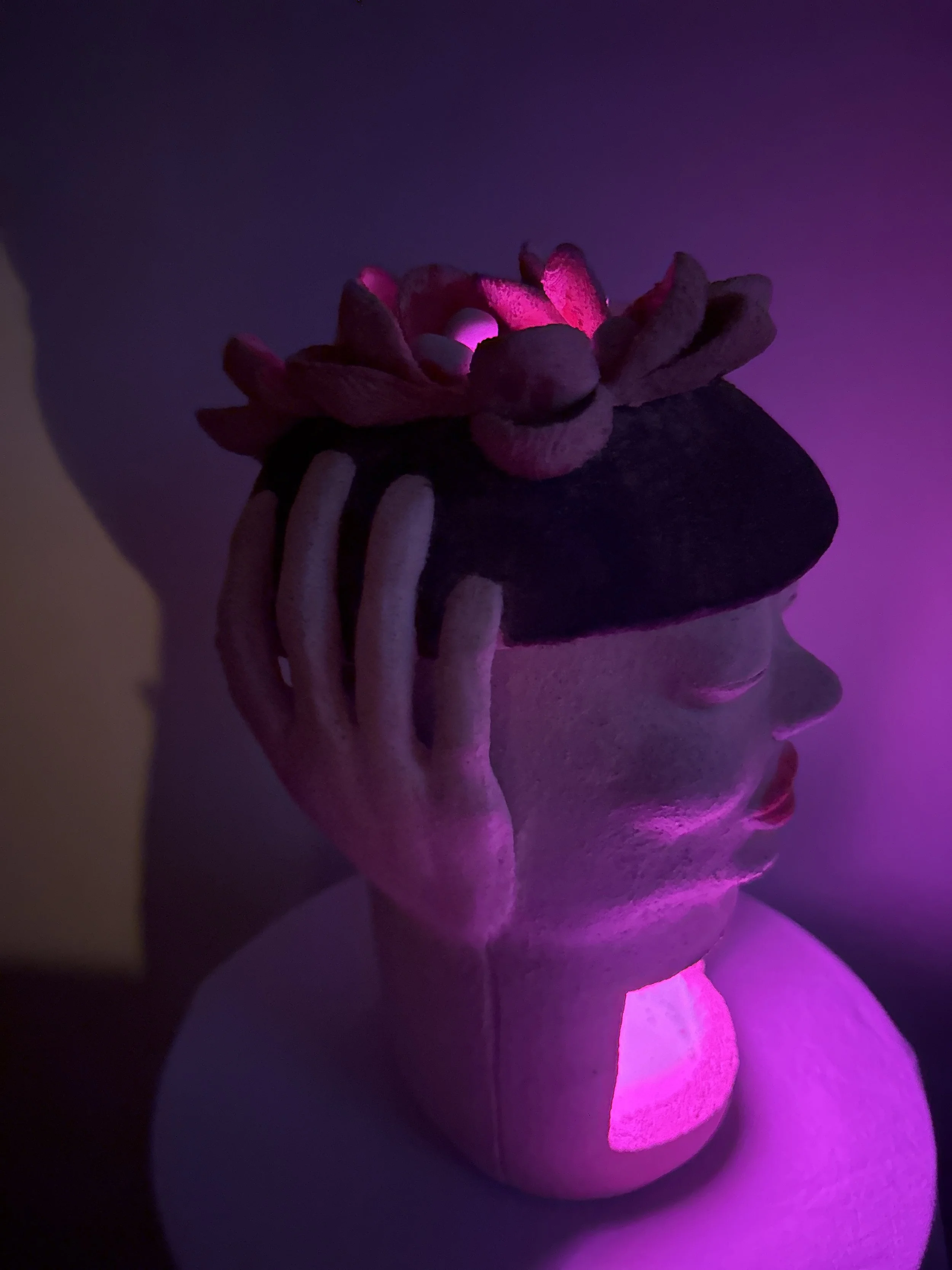 An stoneware ceramic sculpture portrait titled ‘Beret Adjustment’ bathed in soft lavender color from a LED light in it’s interior.