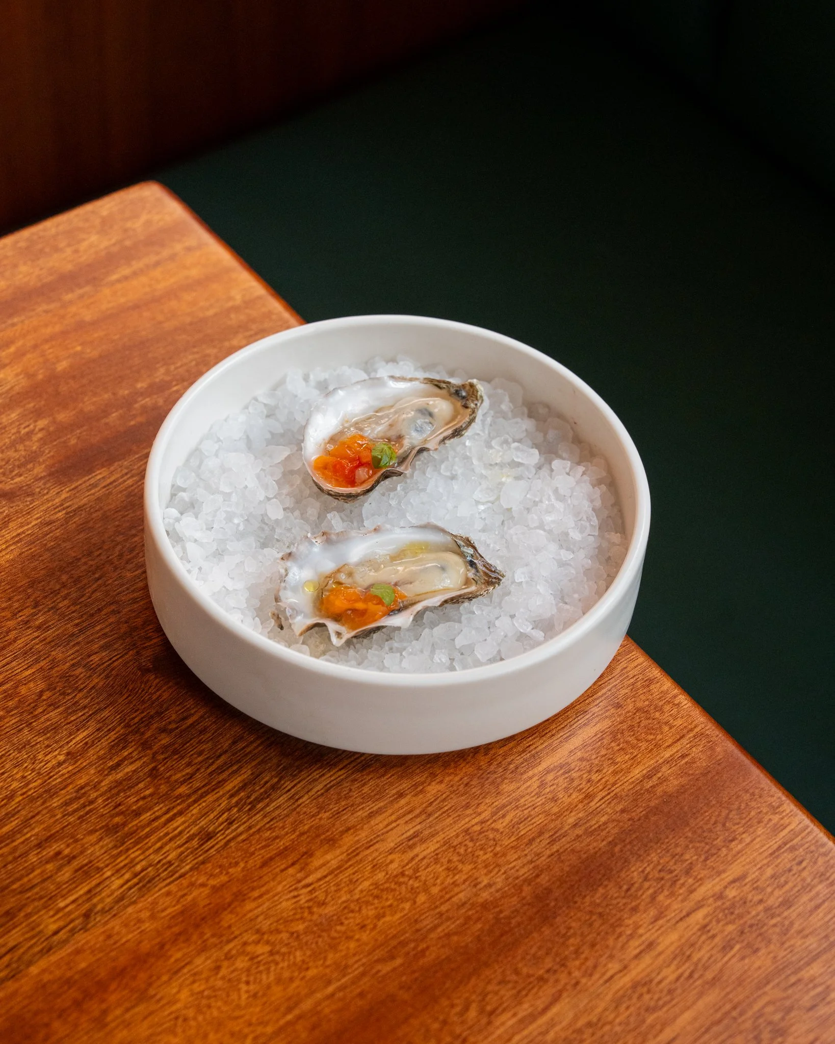 Two oysters on the half shell in a white bowl filled with crushed ice.