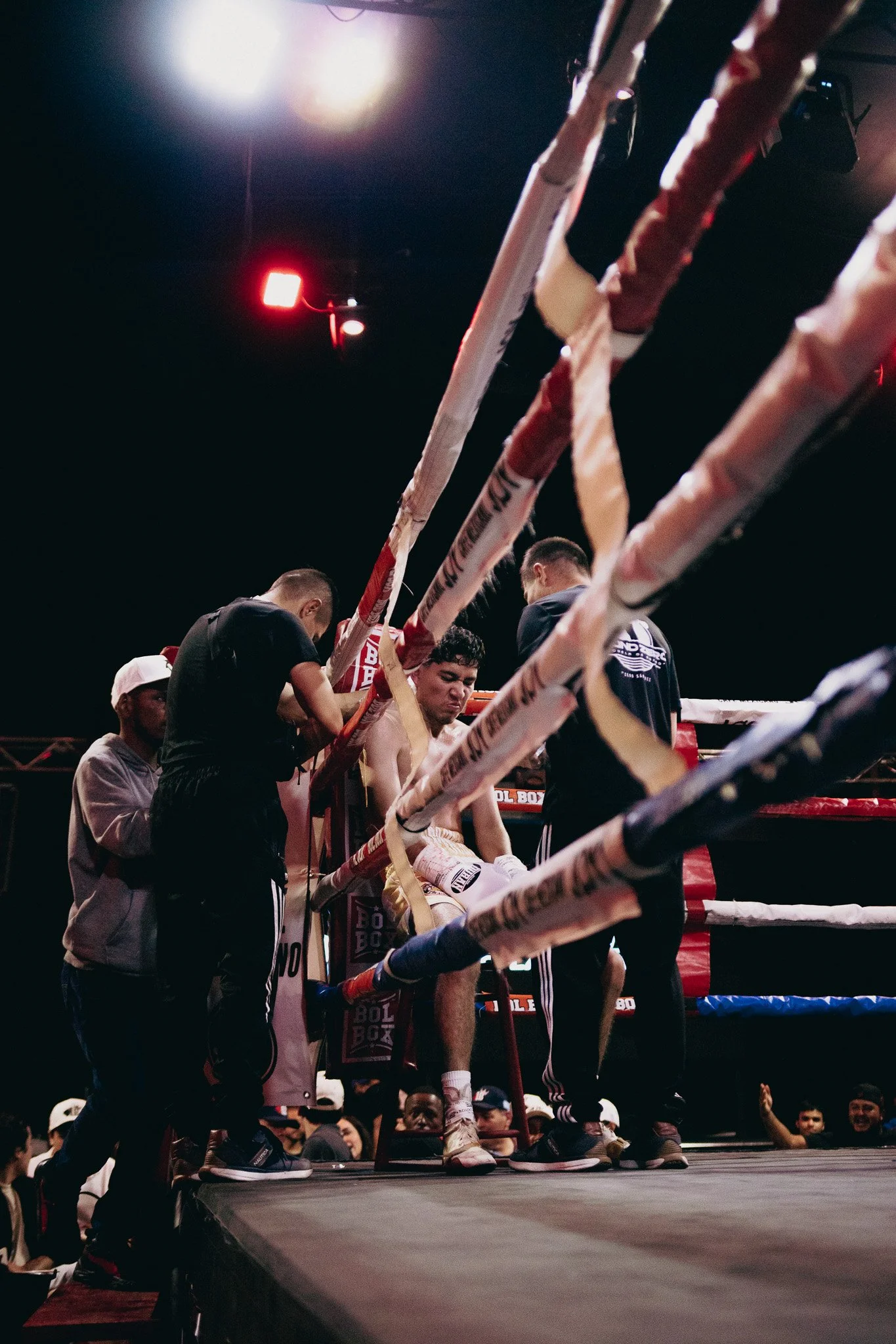 Boxeador en el rincón del ring recibiendo asistencia de su equipo entre round, espectadores en el fondo