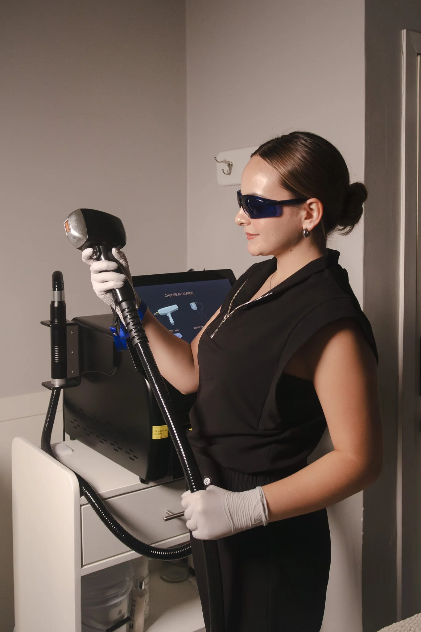 Mujer con gafas de protección y guantes blancos sosteniendo un dispositivo láser en un entorno clínico