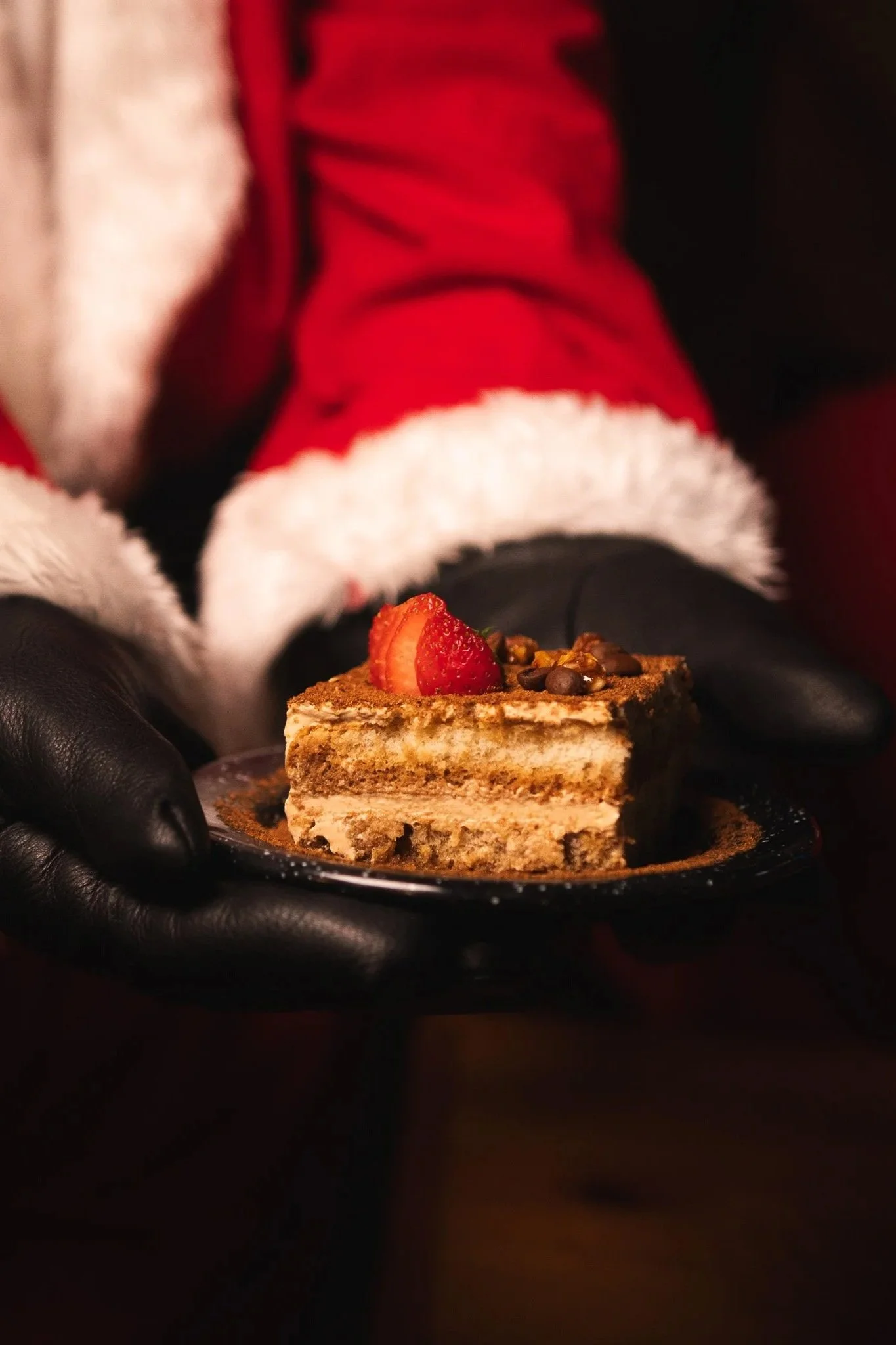 Santa claus sosteniendo un plato con trozo de tiramisú decorado con fresa y nueces.