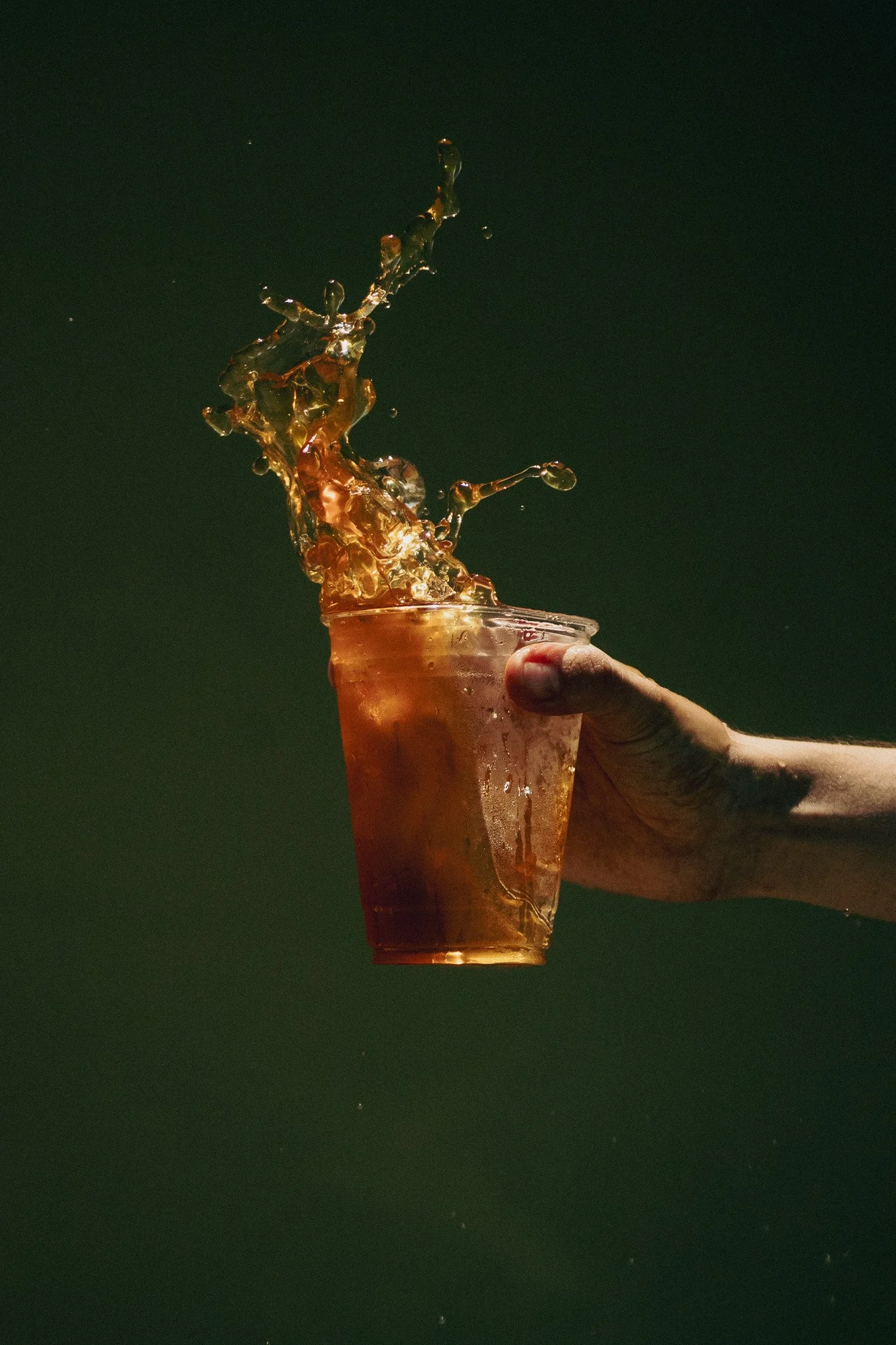 Una mano sostiene un vaso con una bebida de color ámbar, y el líquido salta y crea una explosión en la parte superior del vaso.