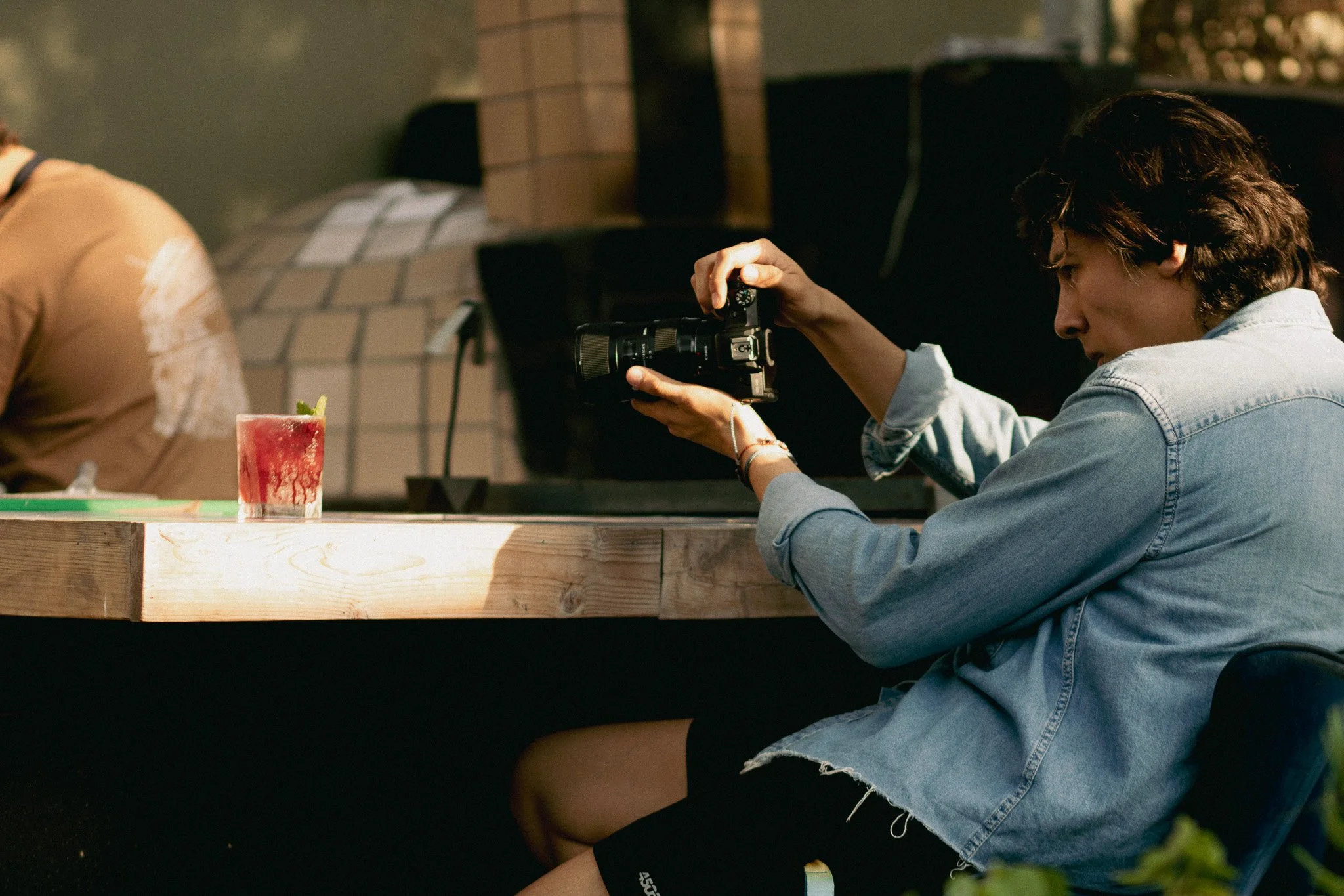 Persona en un establecimiento grabando con cámara mientras tiene un cóctel en una mesa de madera.