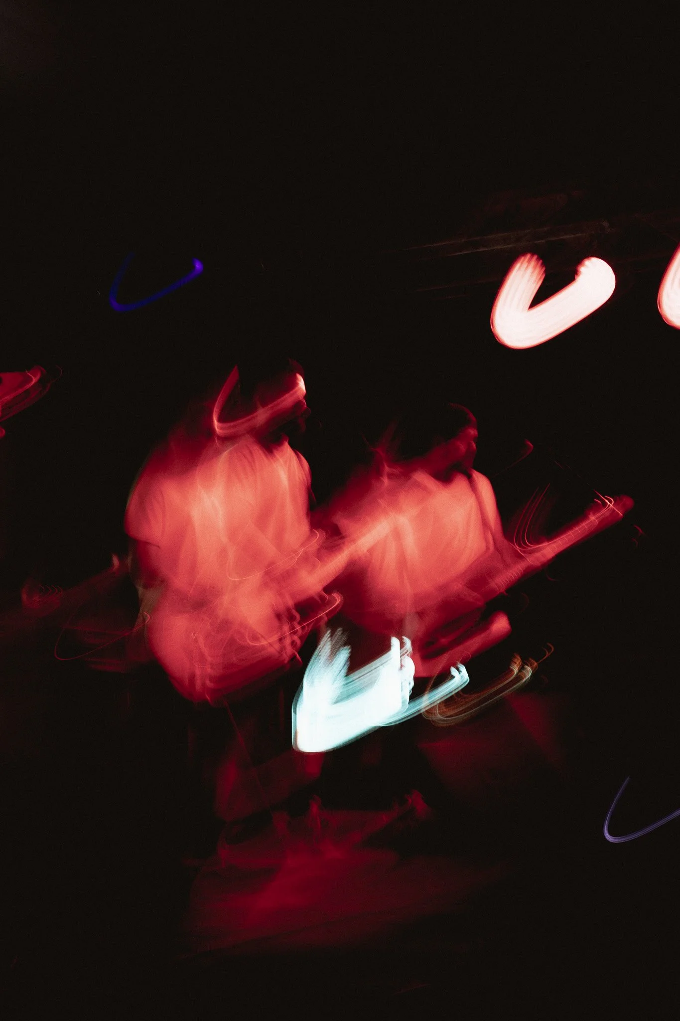 Dos músicos tocando guitarras en un escenario con luces rojas y destellos de movimiento.