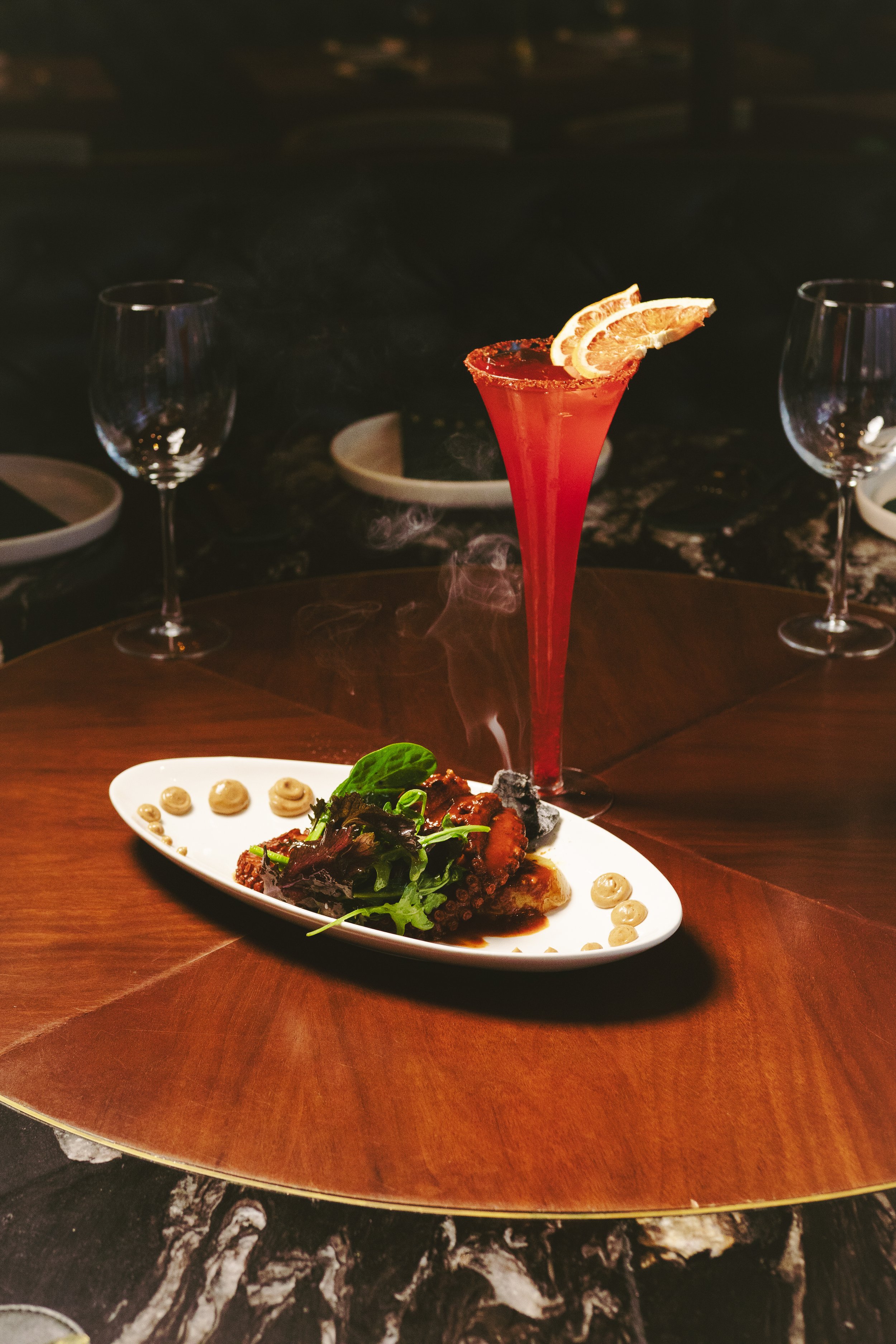 Plato de mariscos acompañado de una bebida roja con rodajas de limón en un ambiente de restaurante elegante.