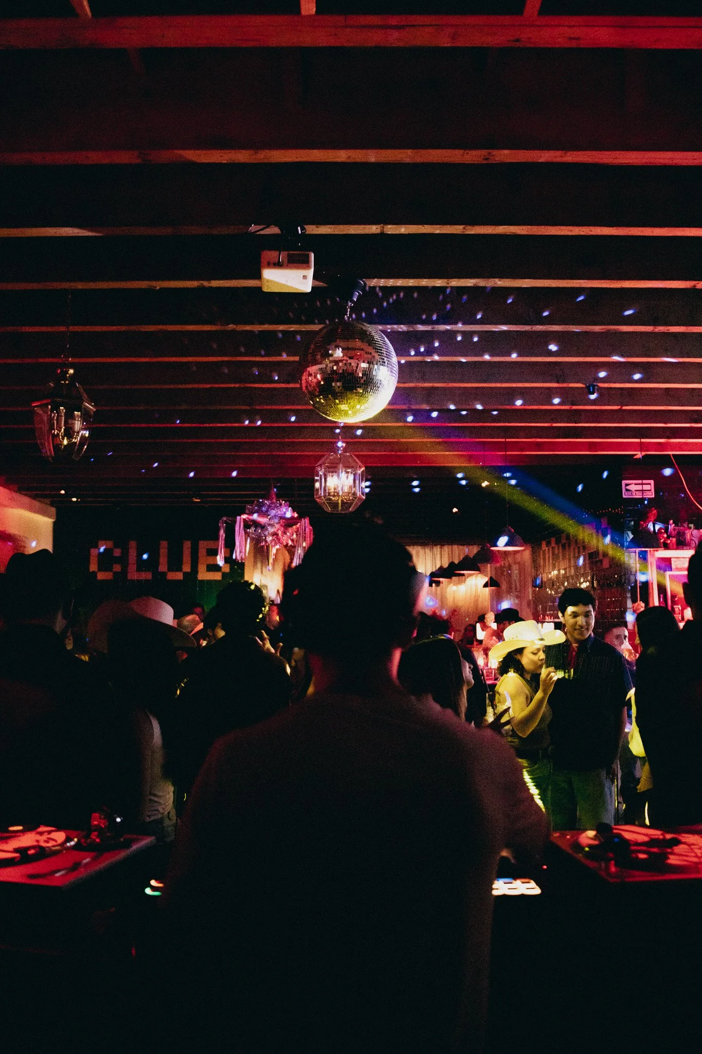 Interior de un club nocturno con personas bailando y socializando, decoración con espejos y luces de discoteca.