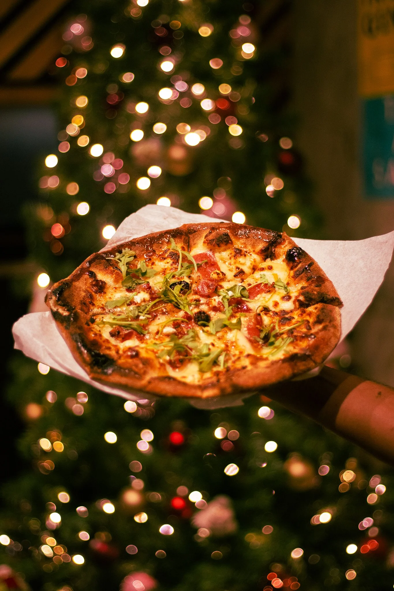 Pizza con vegetales, queso y tocino en un fondo de árbol de Navidad con luces