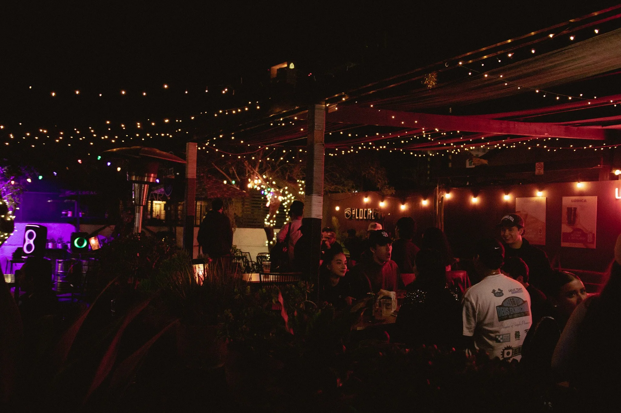 Personas en una terraza con iluminación de luces decorativas y ambiente nocturno.