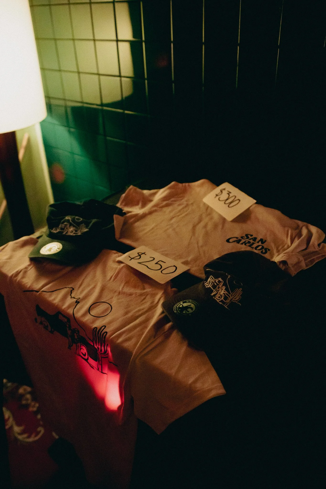 Mesas con camisetas en exhibición y hats con logos en un lugar con decoración moderna.