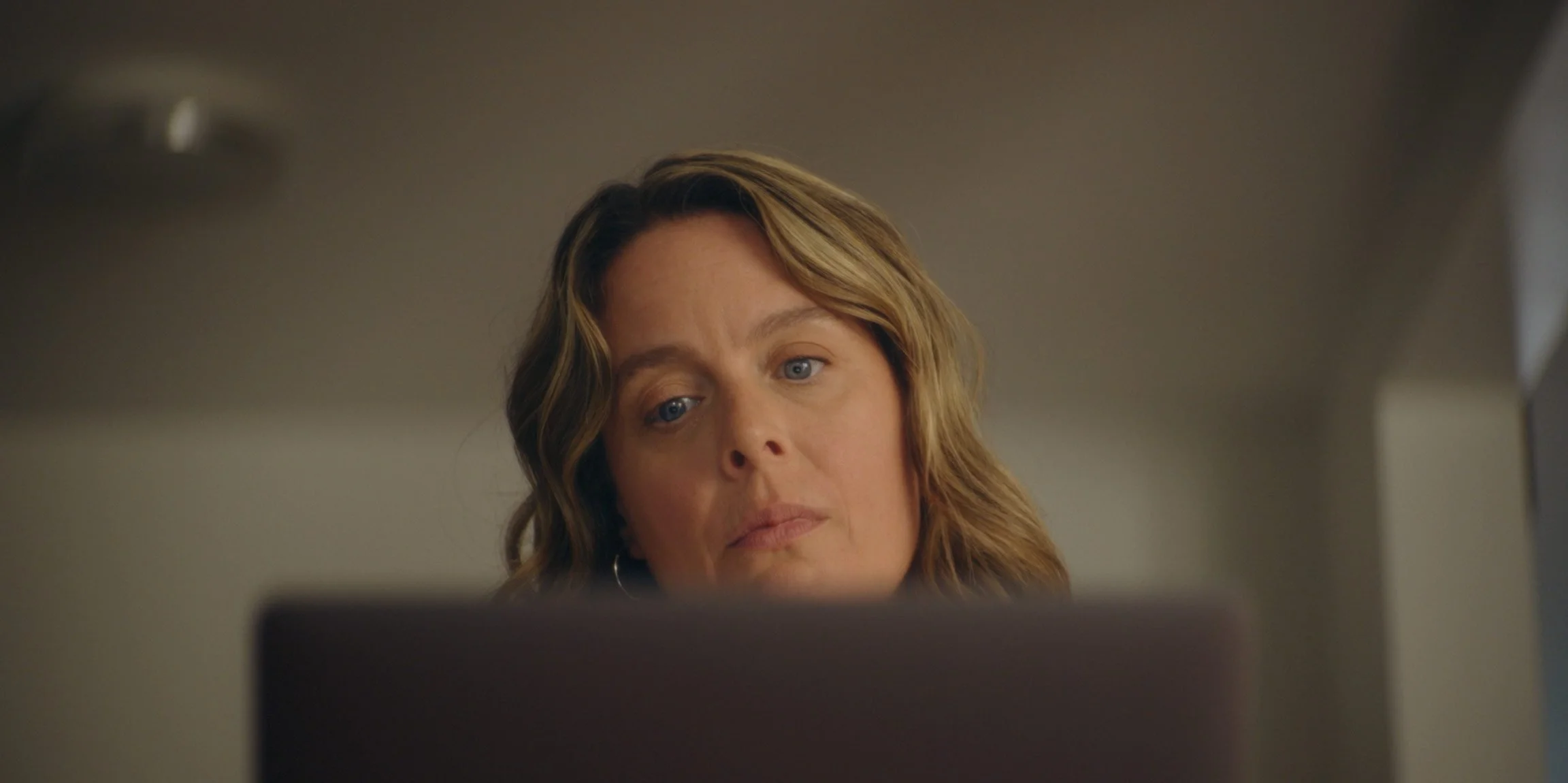 A woman with wavy, light brown hair looking at a laptop or computer screen.