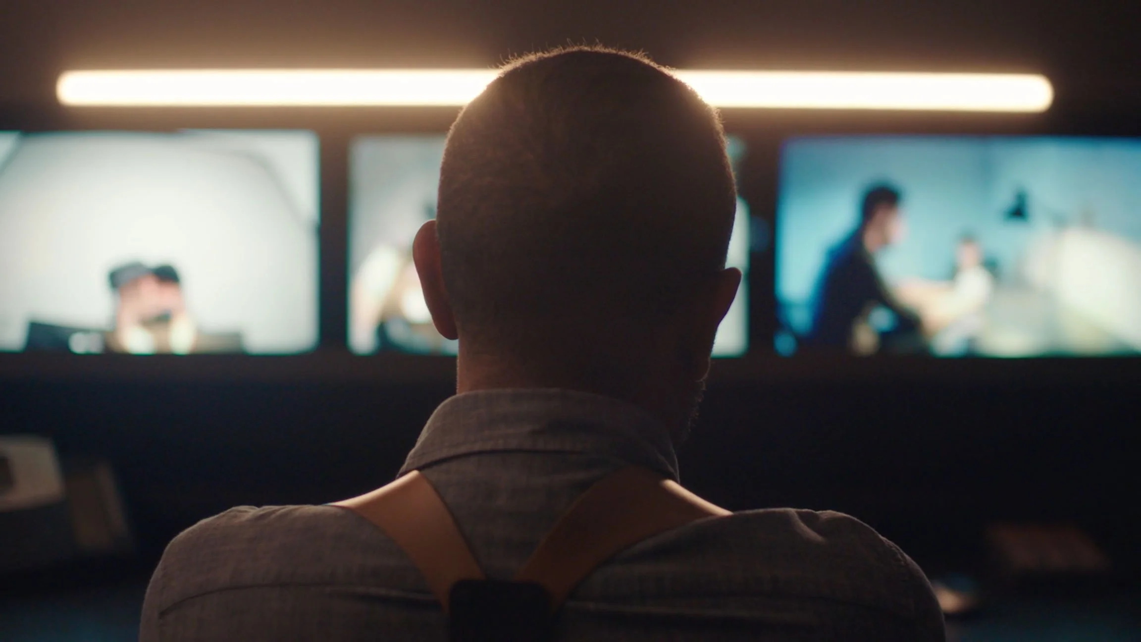 Person with short hair and a collar shirt sitting in front of multiple computer screens, monitoring a virtual meeting.