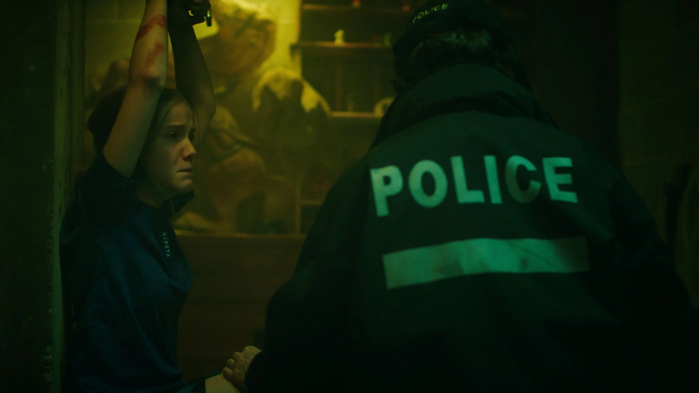 A distressed woman with her hands raised and a police officer confronting her in a dark, tense setting.