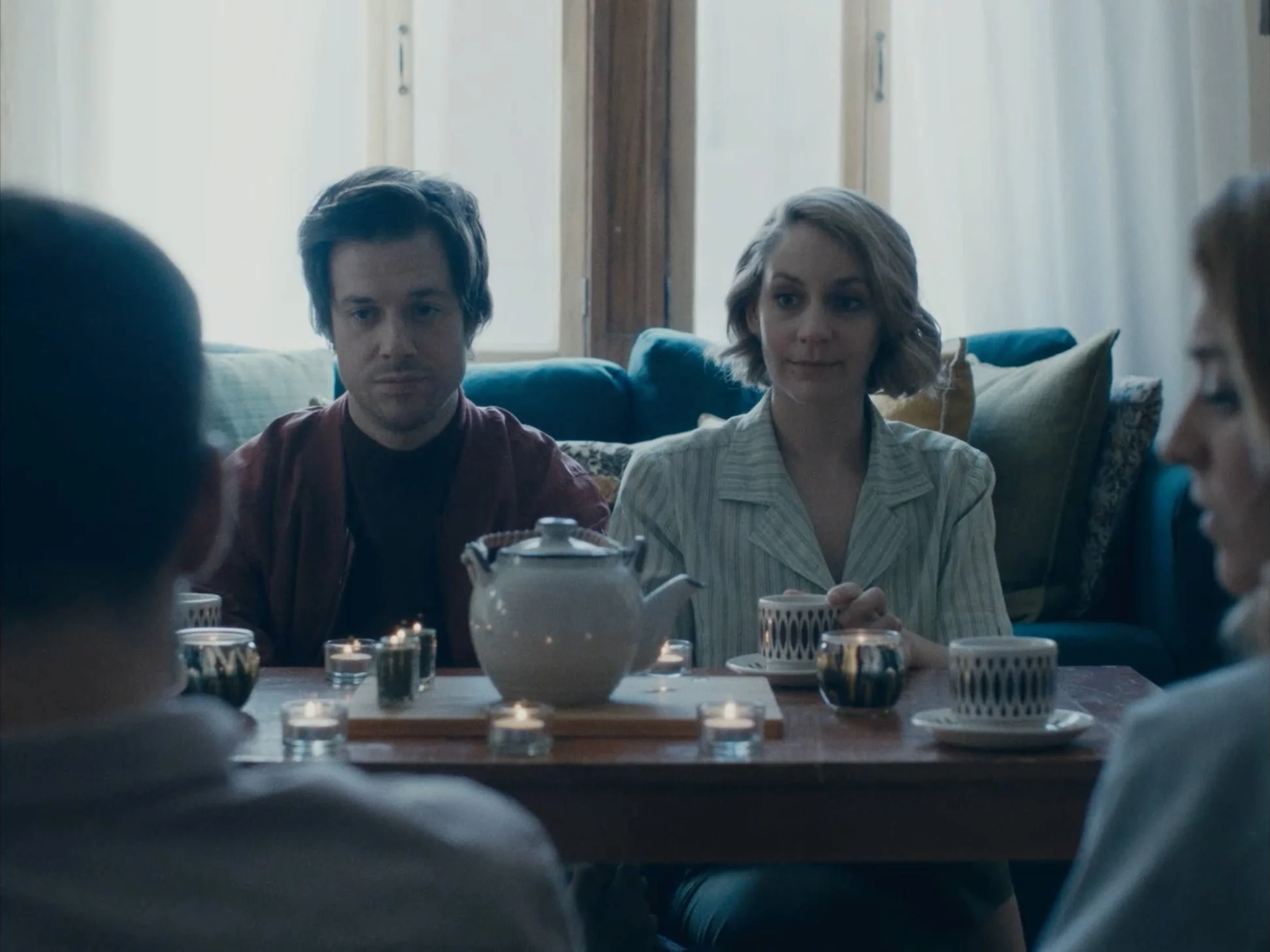 People sitting around a dinner table with teapot and candles in a cozy living room.