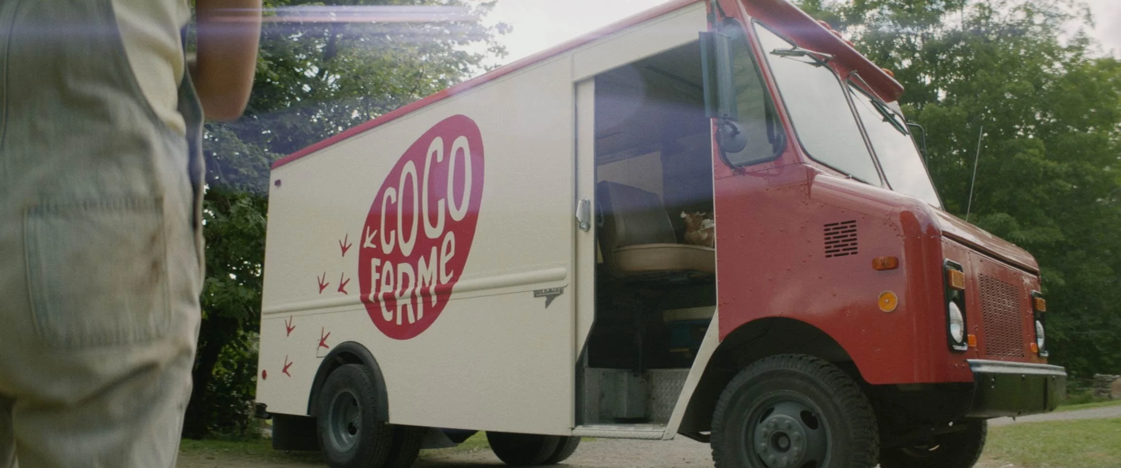 A red and white ice cream truck with a large logo that reads "Coco Farms" parked on a grassy area with trees in the background.