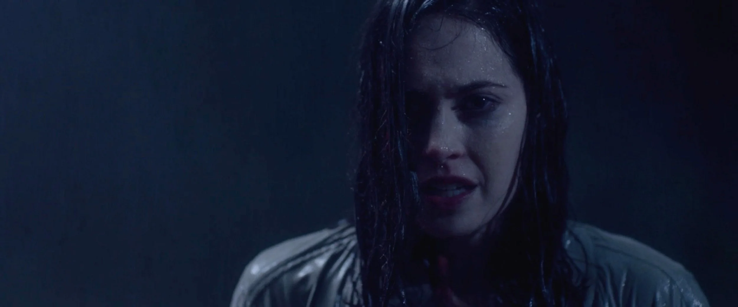 Close-up of a woman with wet hair, dark background, and intense expression.