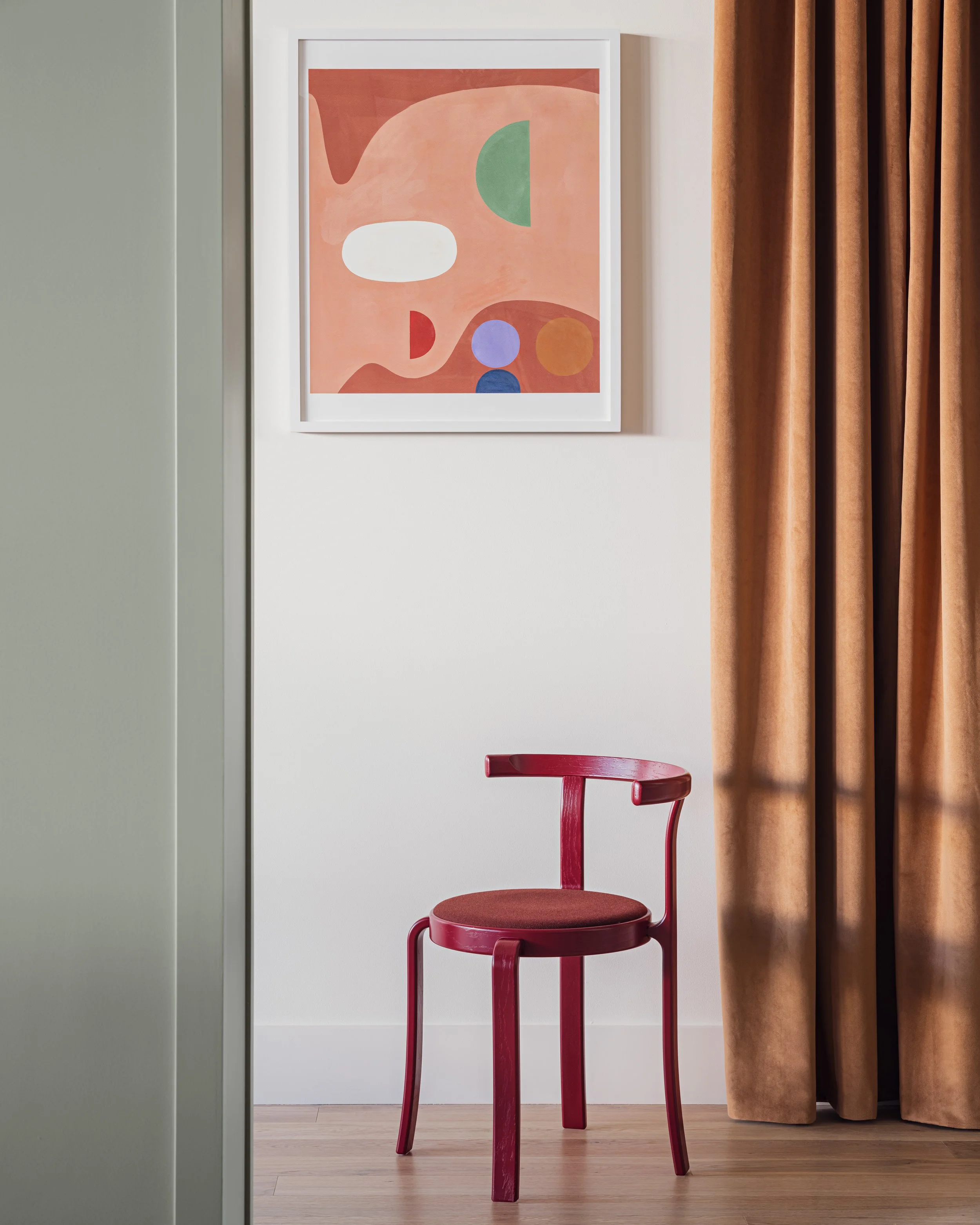 A detail image of a burgundy dining chair in front of custom artwork and drapery at DeLille En Ville.