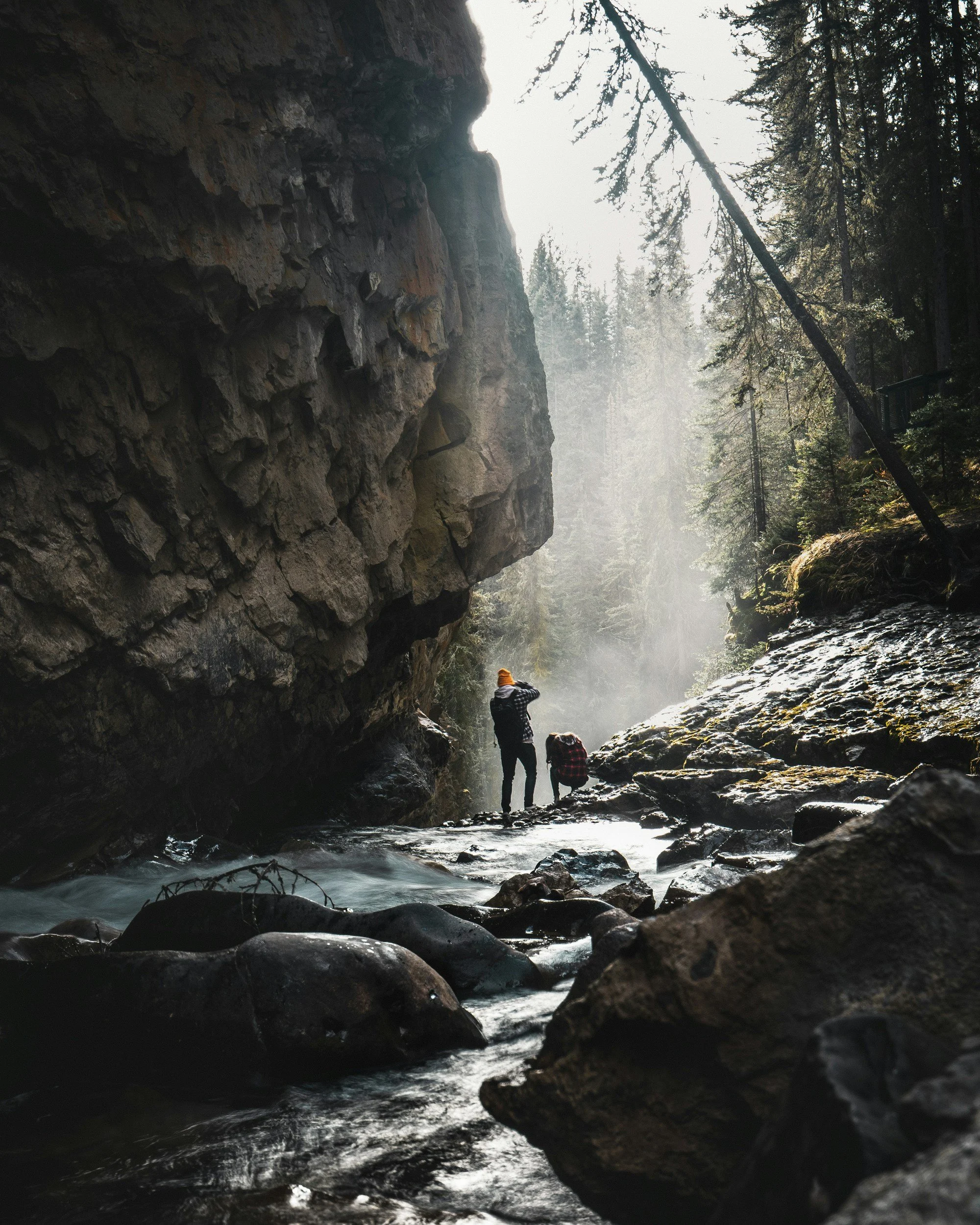 person standing in a creek next to a big rock