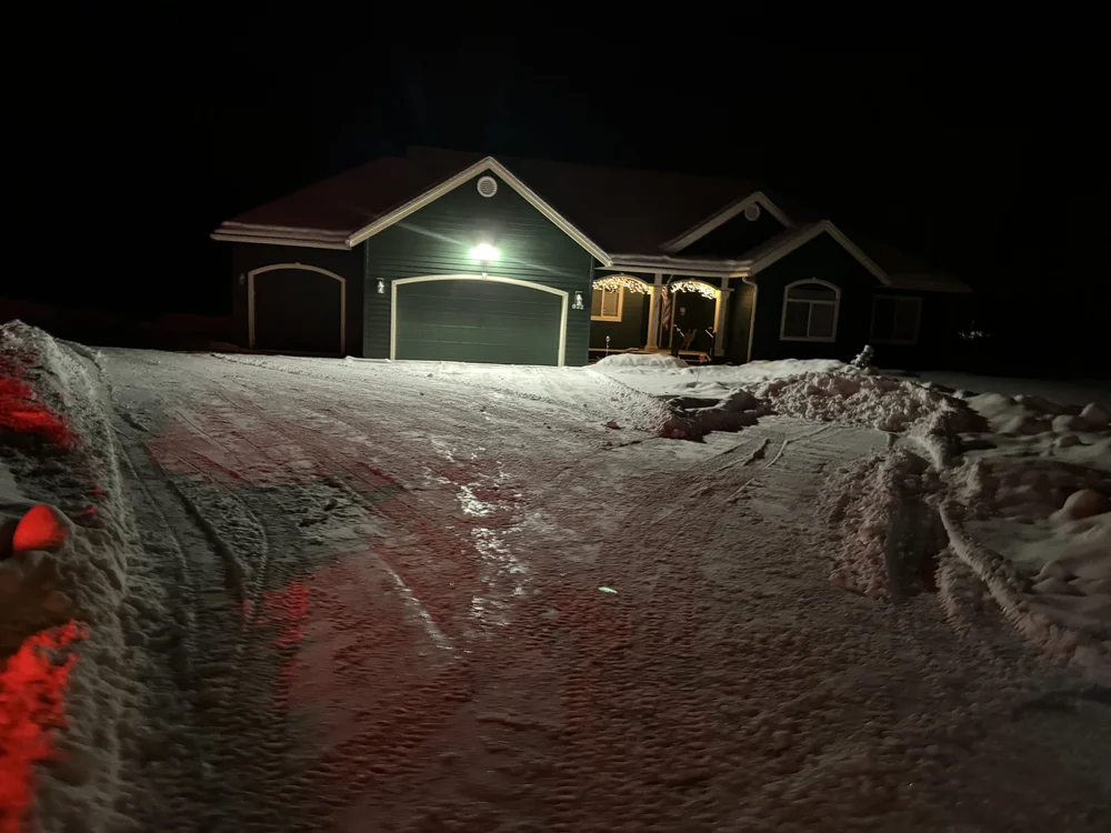 House with exterior lights on and a plowed driveway at night in Palmer, Alaska