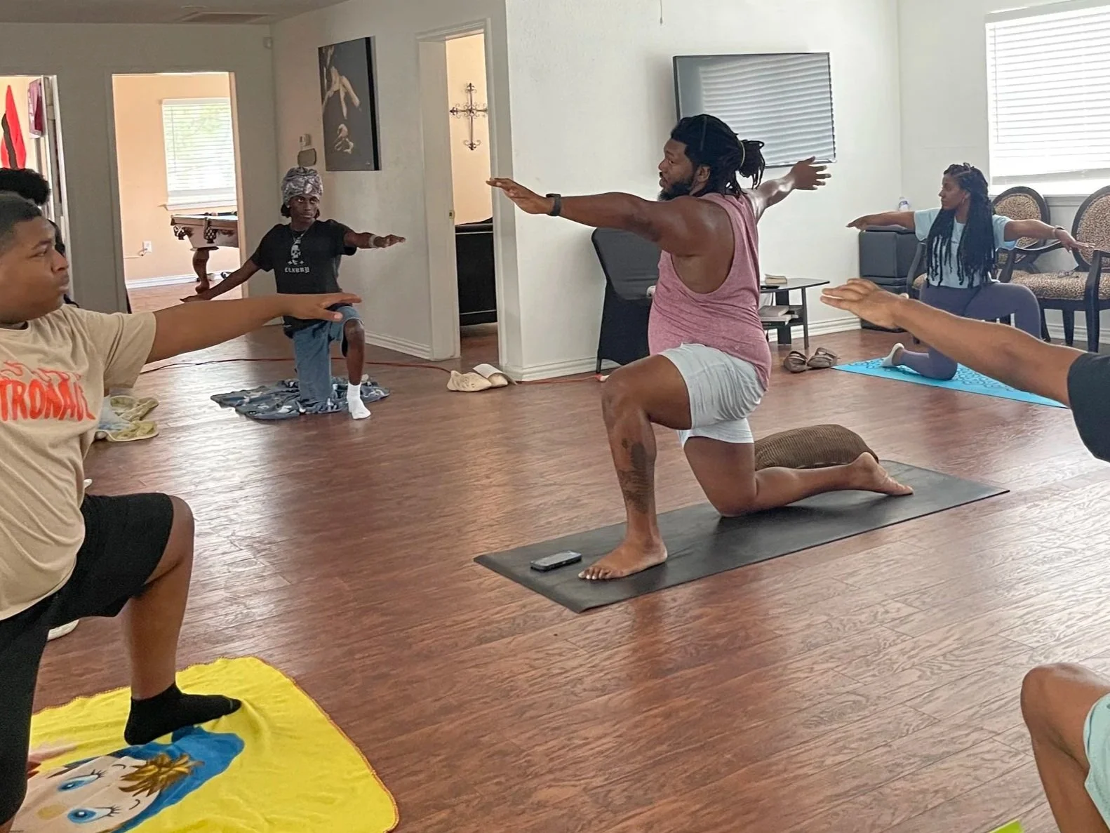 Group of people participating in a yoga class in a studio, with one instructor demonstrating a lunge pose.