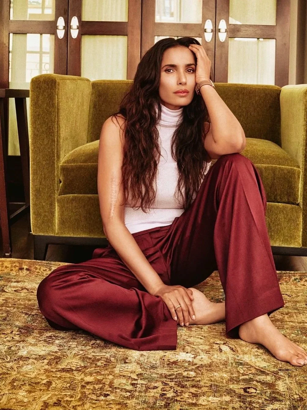 padma lakshmi for Marie claire wearing a light pink sleeveless modal turtleneck and burgundy trousers against a gold velvet chair