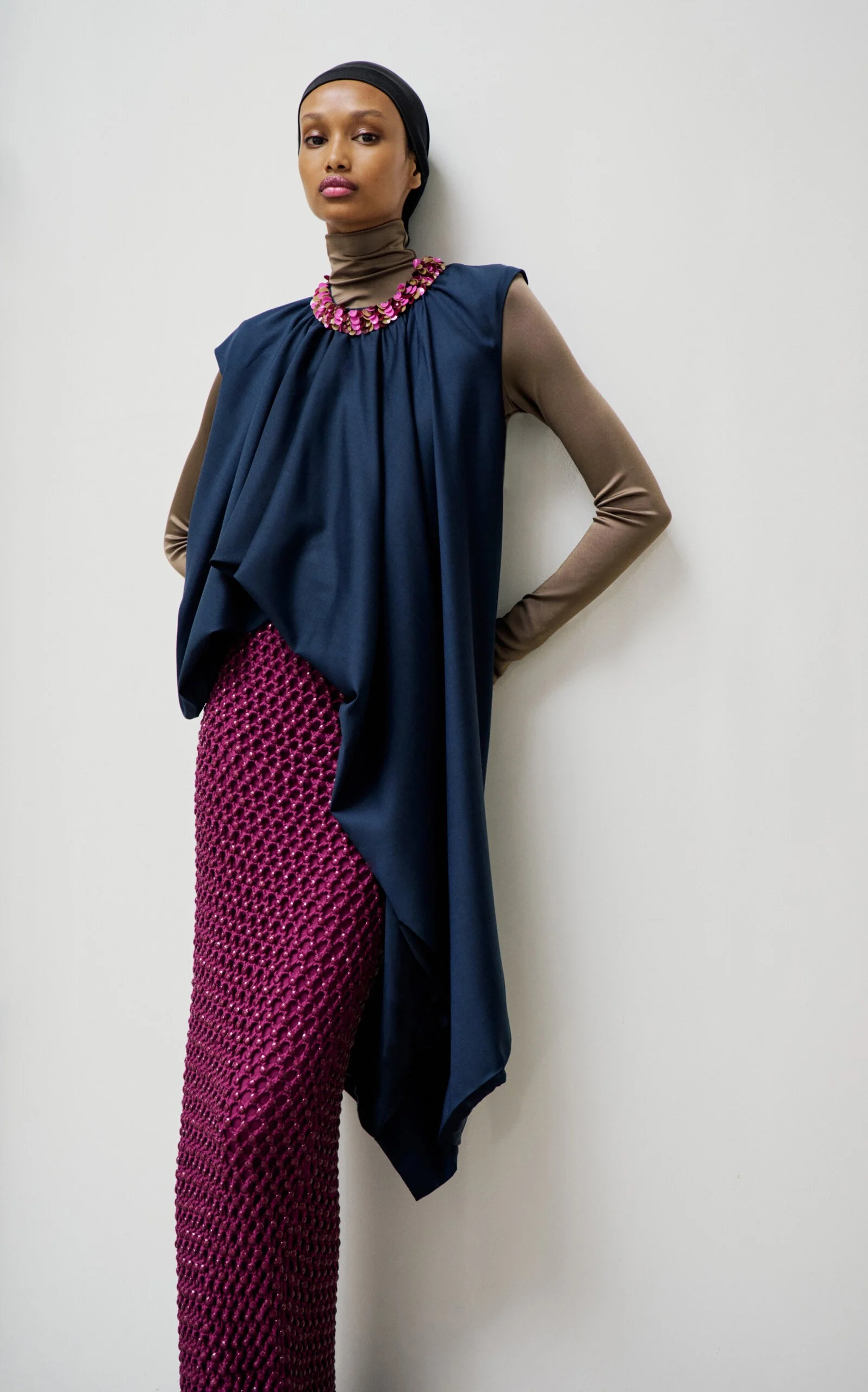Model wearing a fushia purple fishnet overlay skirt and dark navy draped top styled over a sheer taupe turtleneck