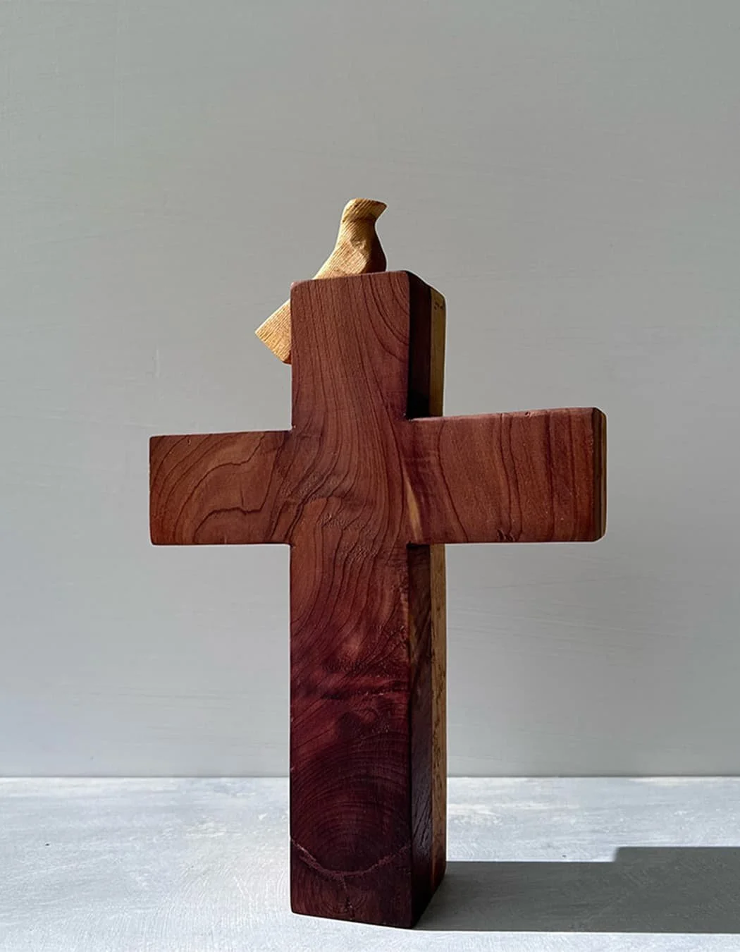 wooden cross with a small carved bird perched on top, made from contrasting light and dark wood