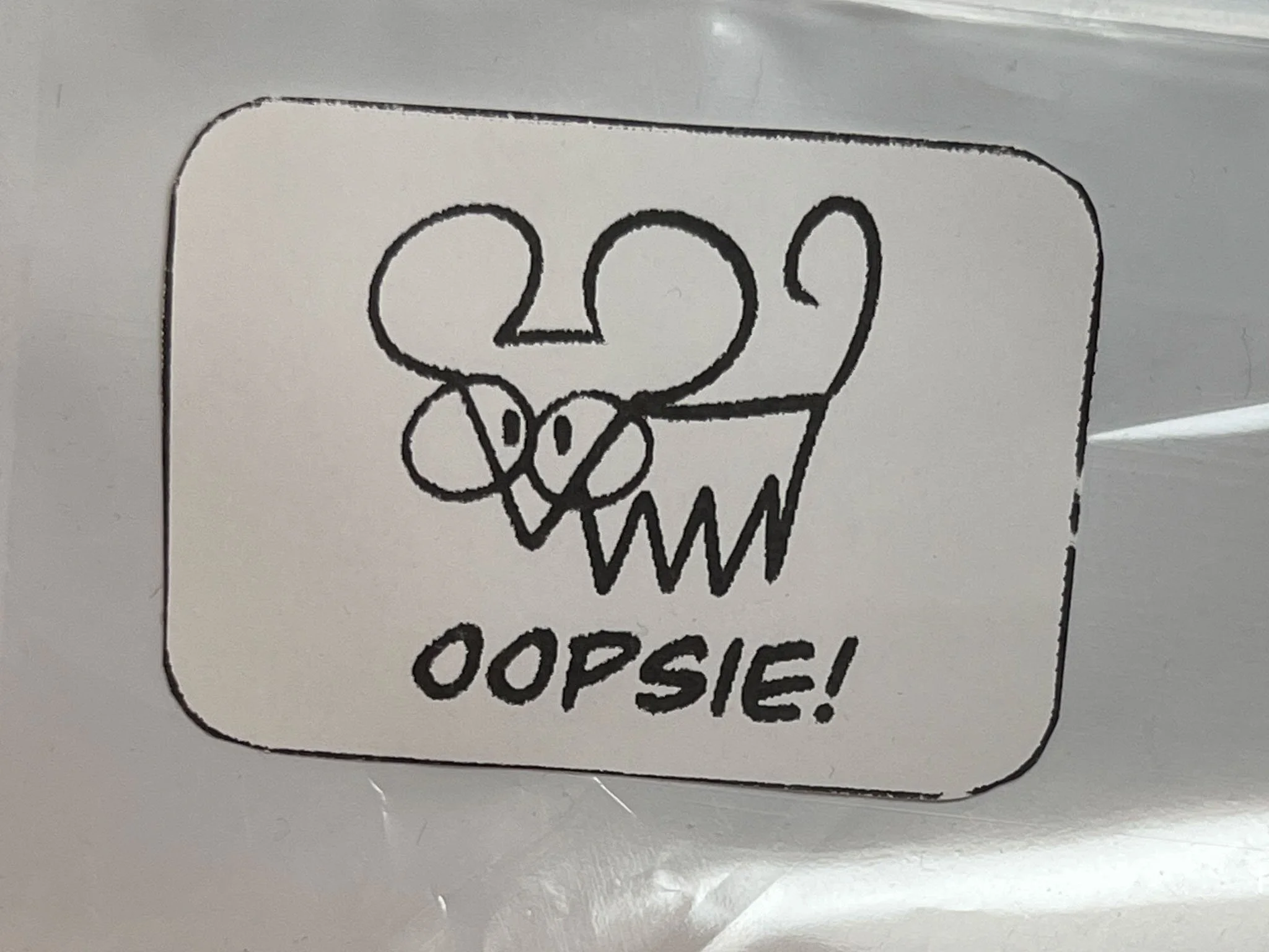 A photo of a white sticker depicting a crude drawing of a rat with glasses above the text "OOPSIE!"