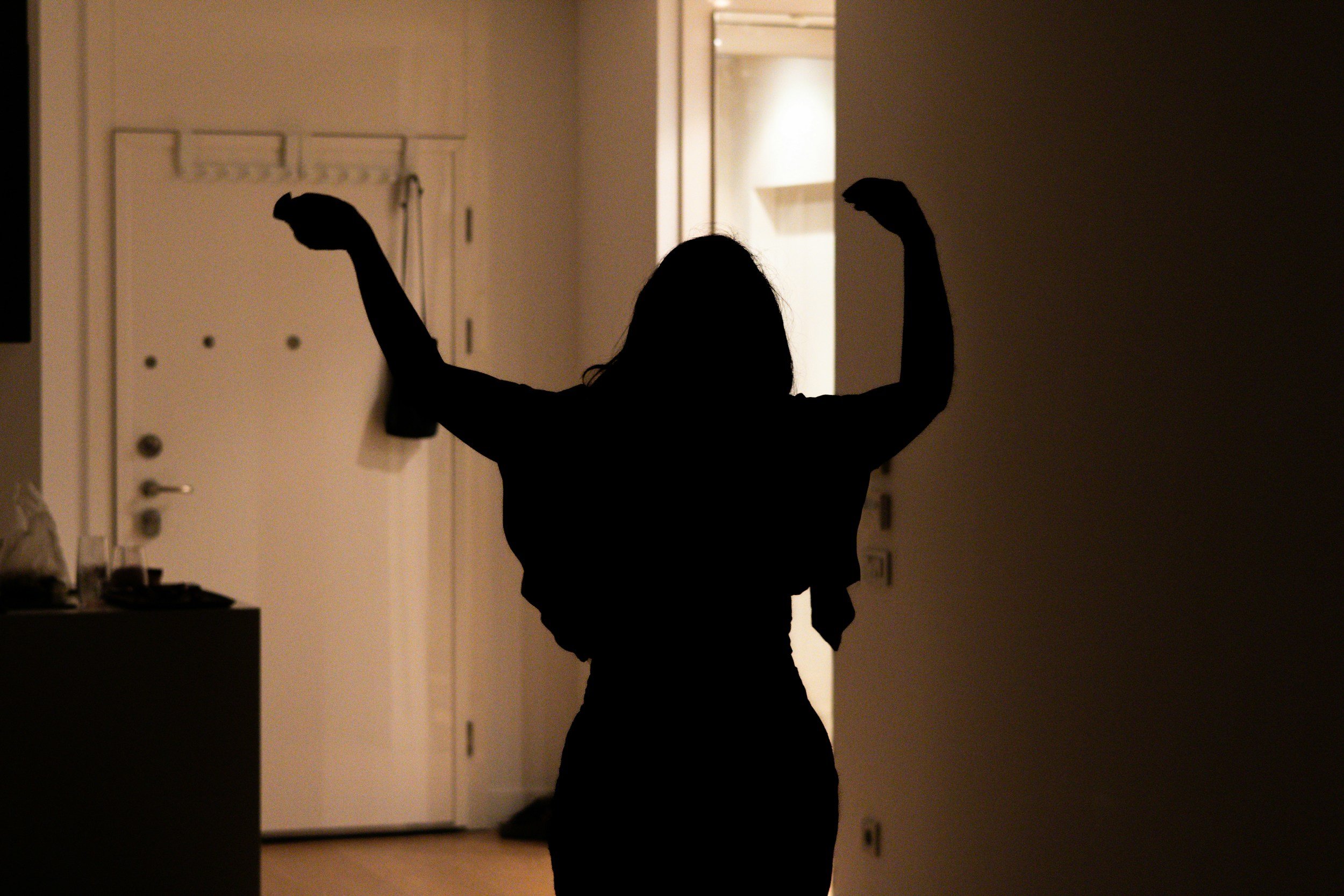 Silhouette of a woman flexing her arms in a dimly lit room.