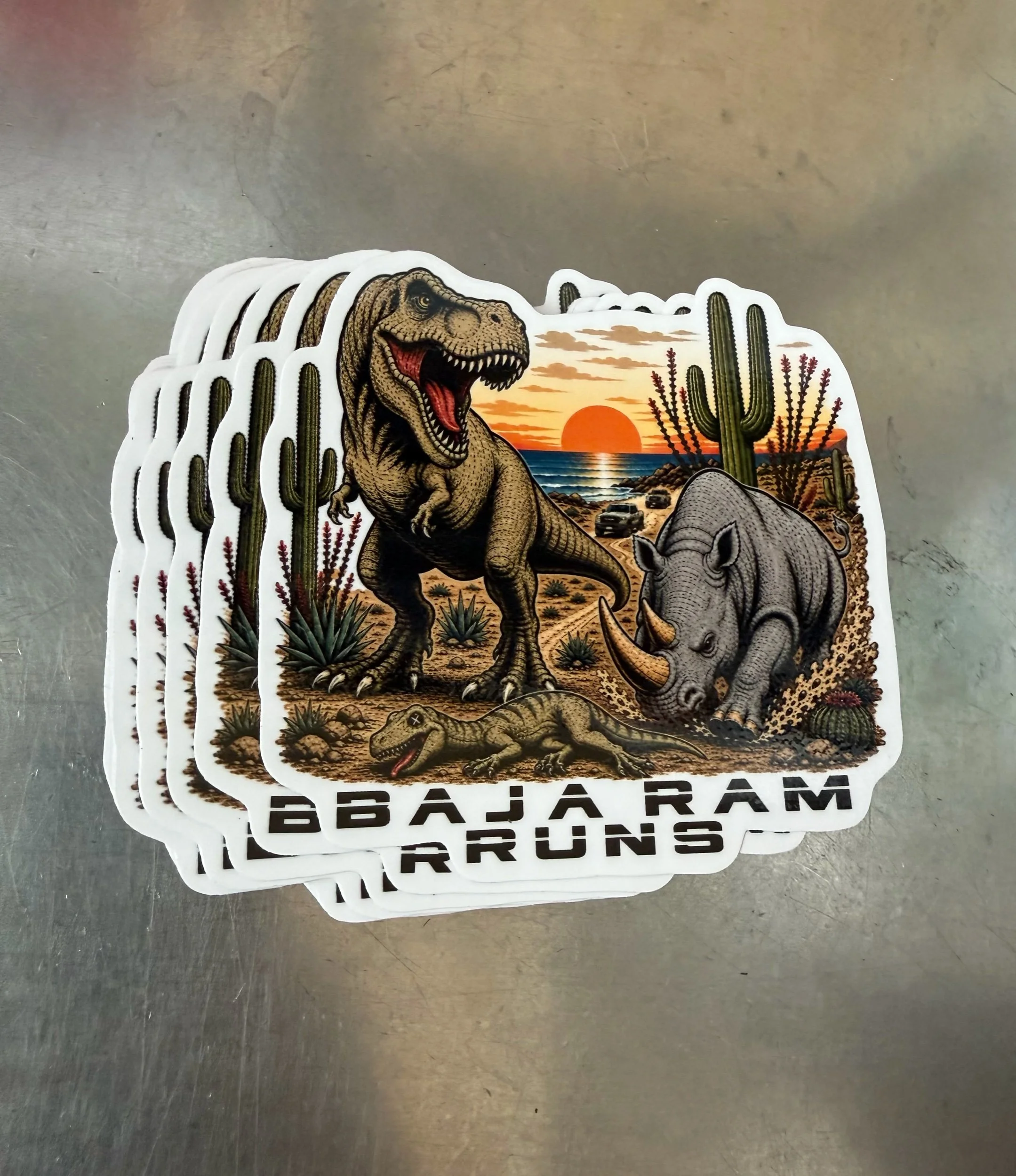 4-inch Baja Ram Runs Apex Predator gloss vinyl decal with T. rex, rhino, Ram trucks, and Baja-inspired desert artwork.