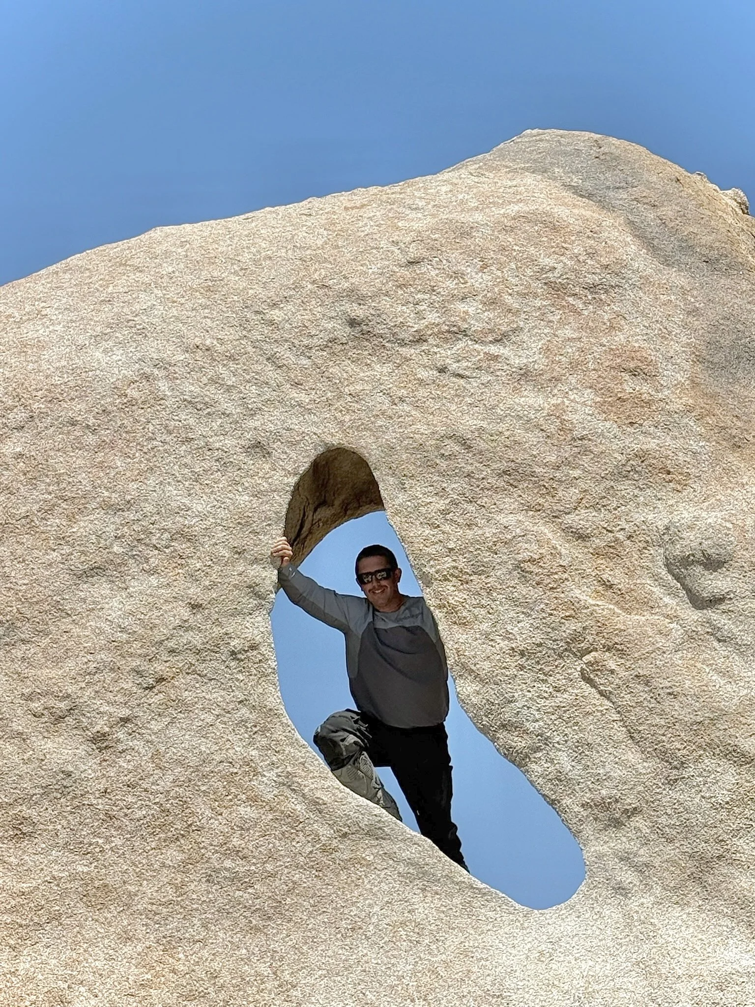 Man exploring Window Rock in Baja, Mexico, standing through a natural granite rock formation under a clear blue sky.