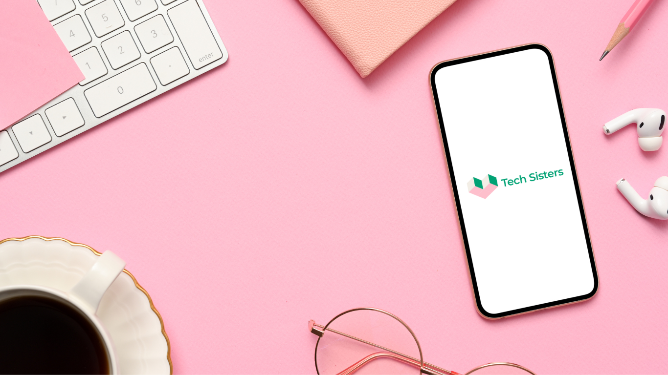 Ett rosa skrivbord fotat ovanifrån, ett par glasögon och en telefon med Tech Sisters logoyp på skärmen.