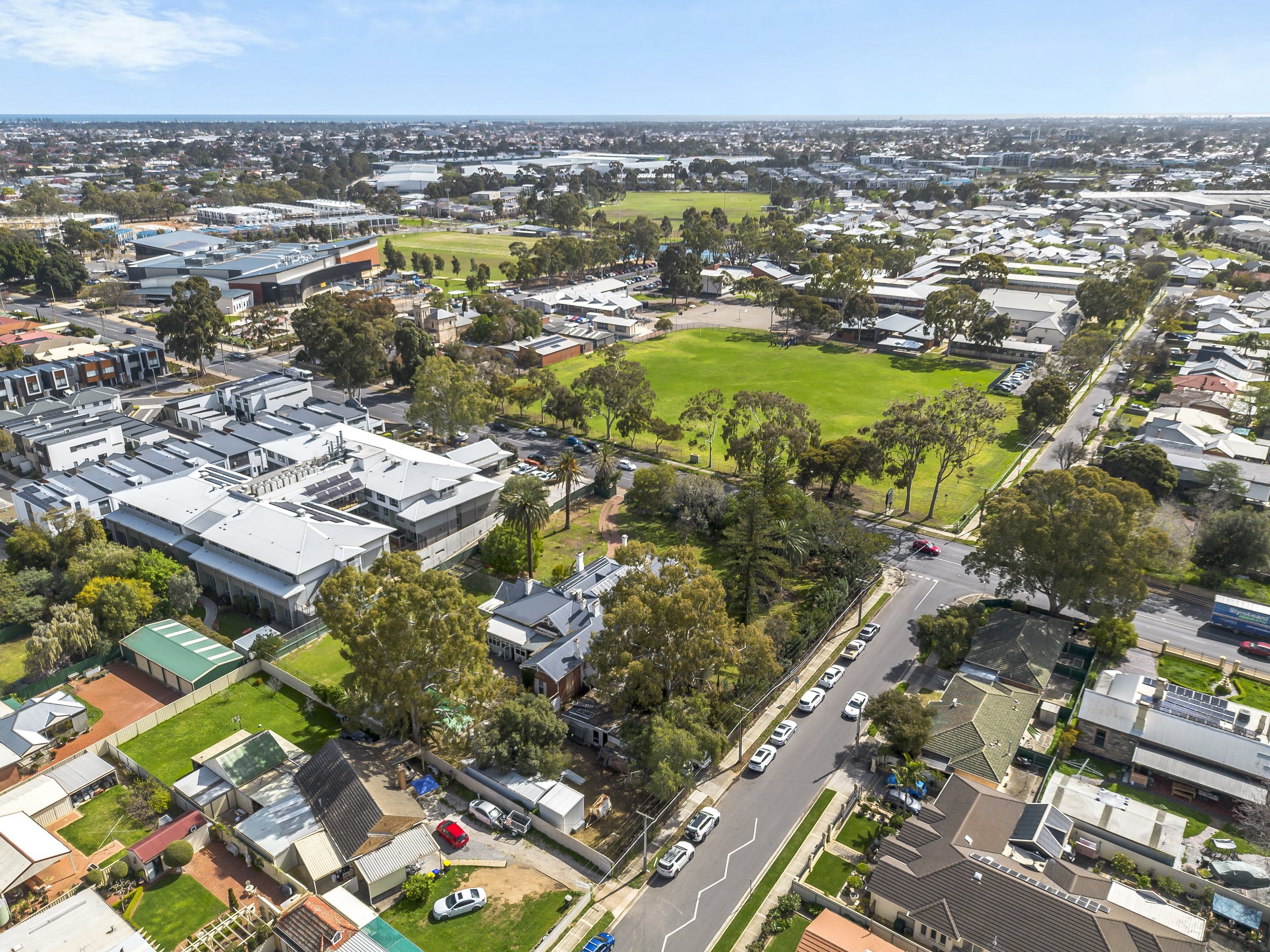 Aerial view of a suburban neighborhood with residential houses, a large grassy park, and surrounding trees.