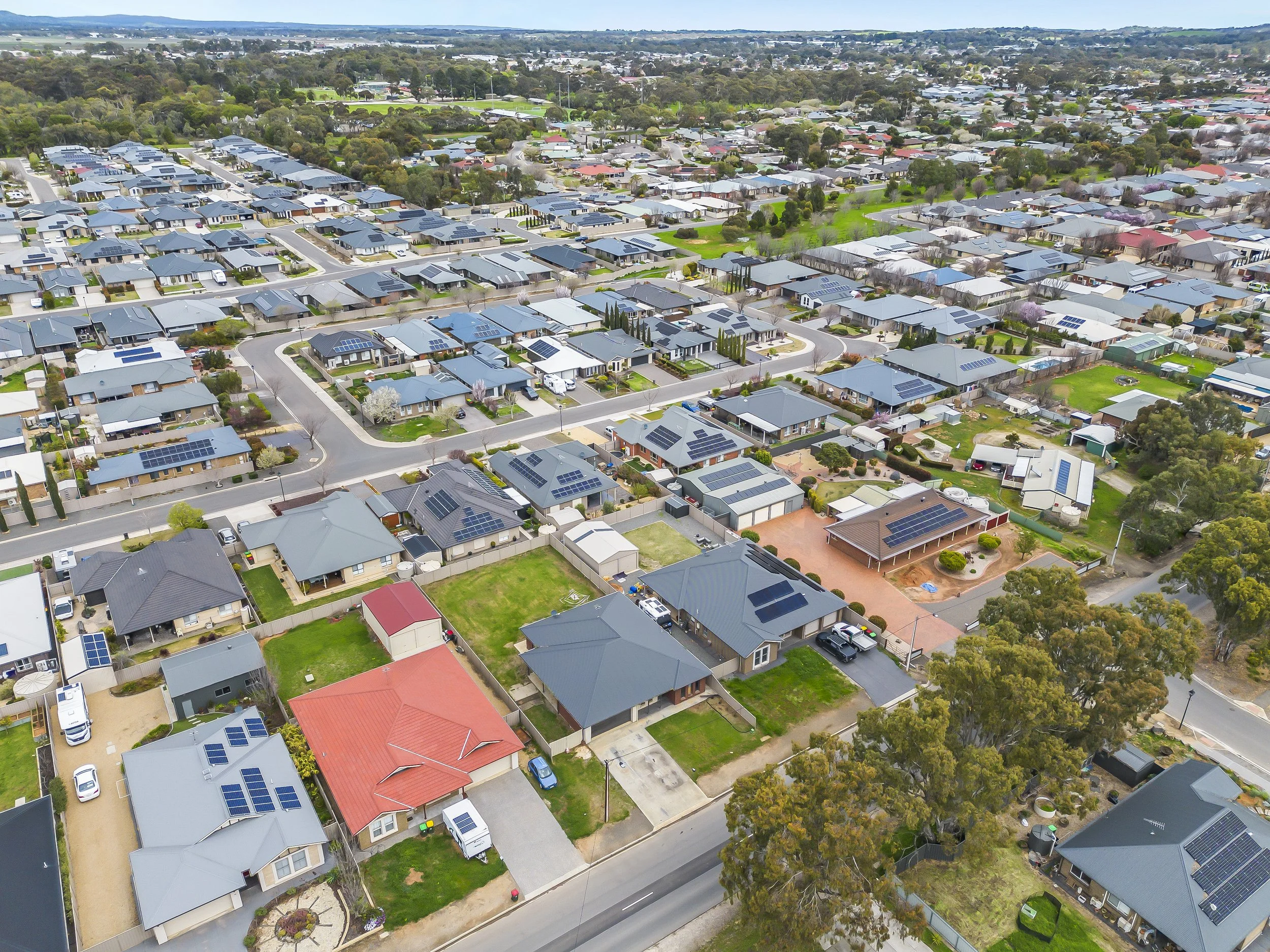 Aerial view of a suburban neighborhood with houses featuring solar panels on roofs, green lawns, and tree-lined streets.