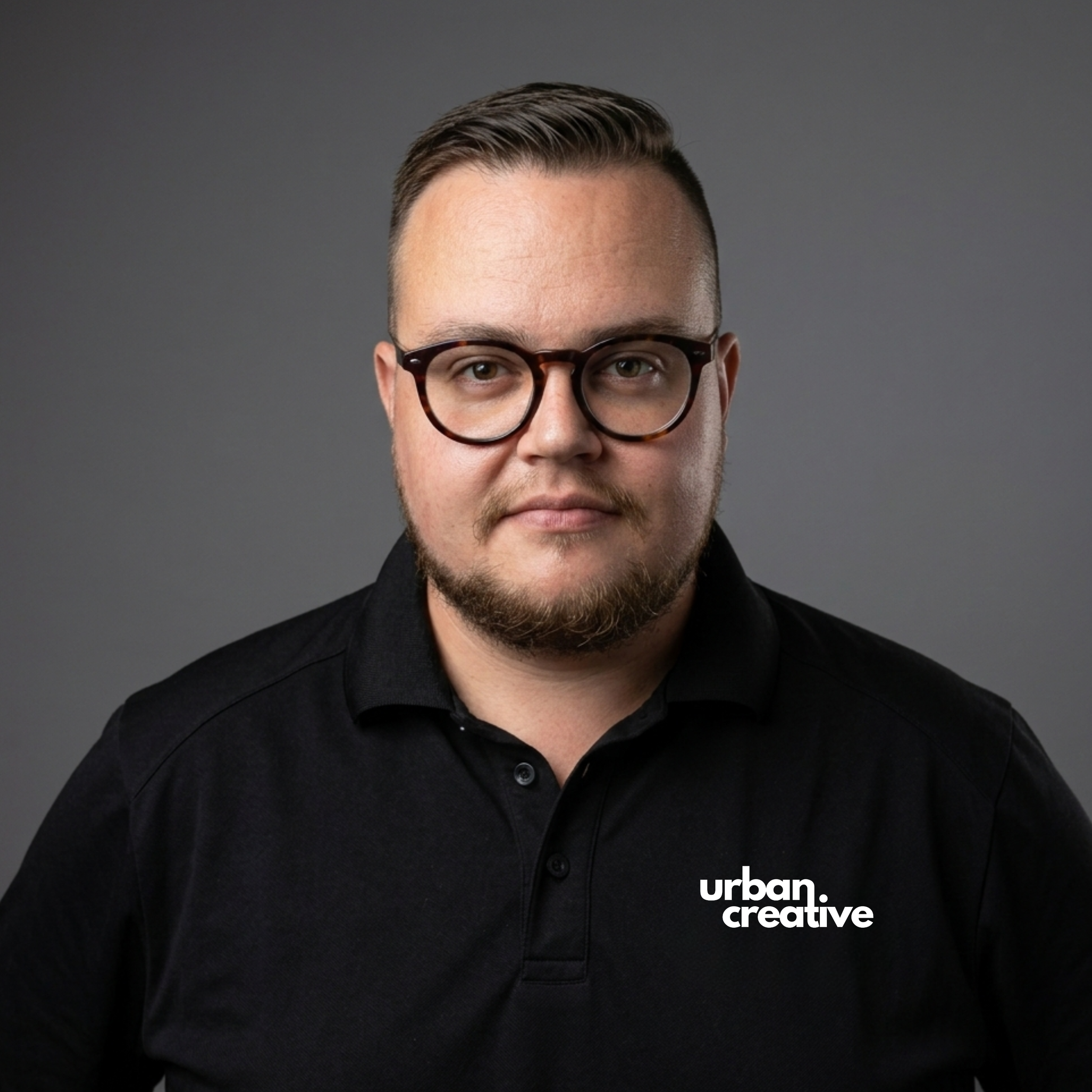 Close-up of a man's face wearing glasses, dressed in a black shirt, with a plain gray background. The words 'urban creative' are written in white at the bottom right corner.
