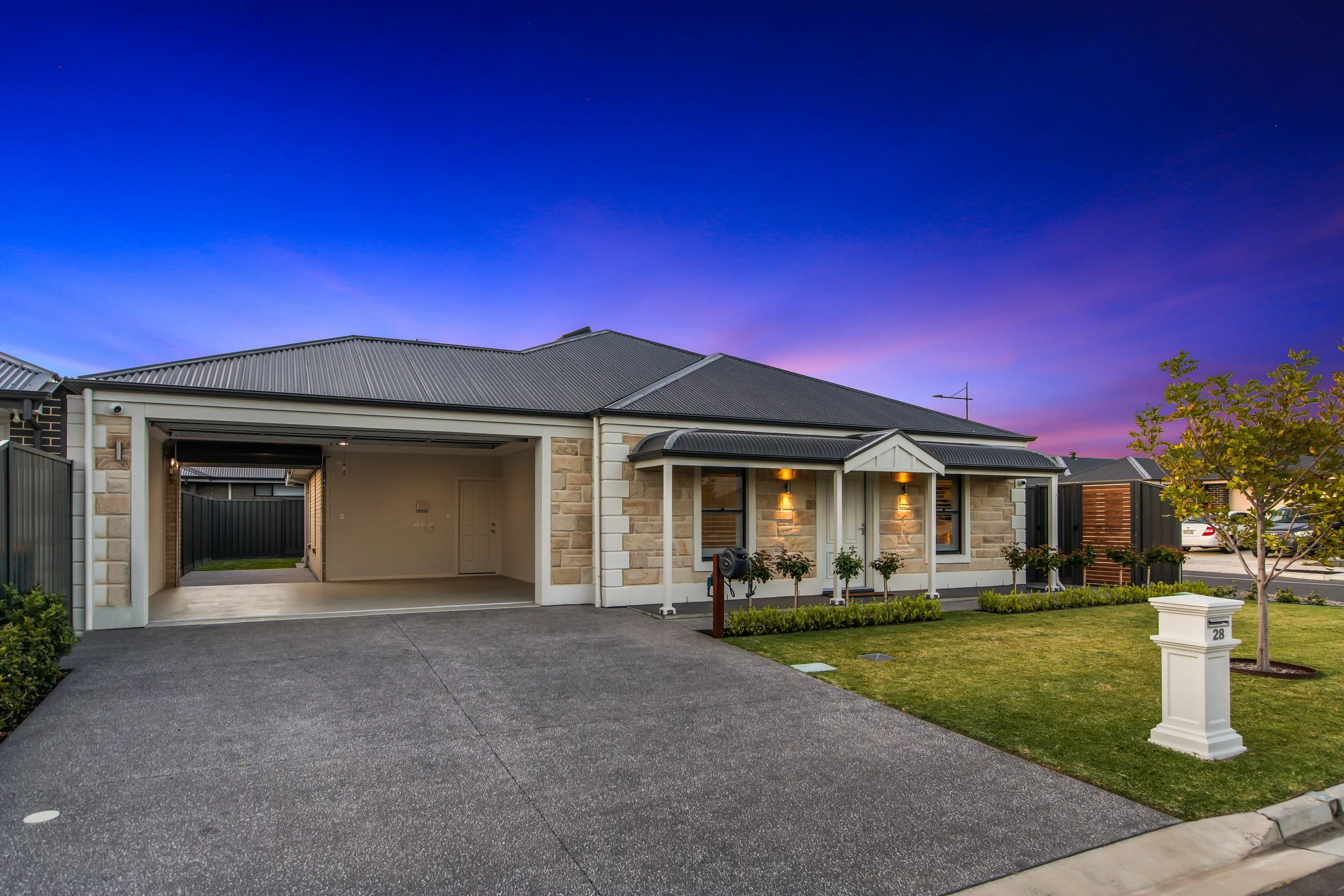 Modern suburban house with a attached garage, manicured lawn, small tree, and a mailbox with the number 28, during twilight.
