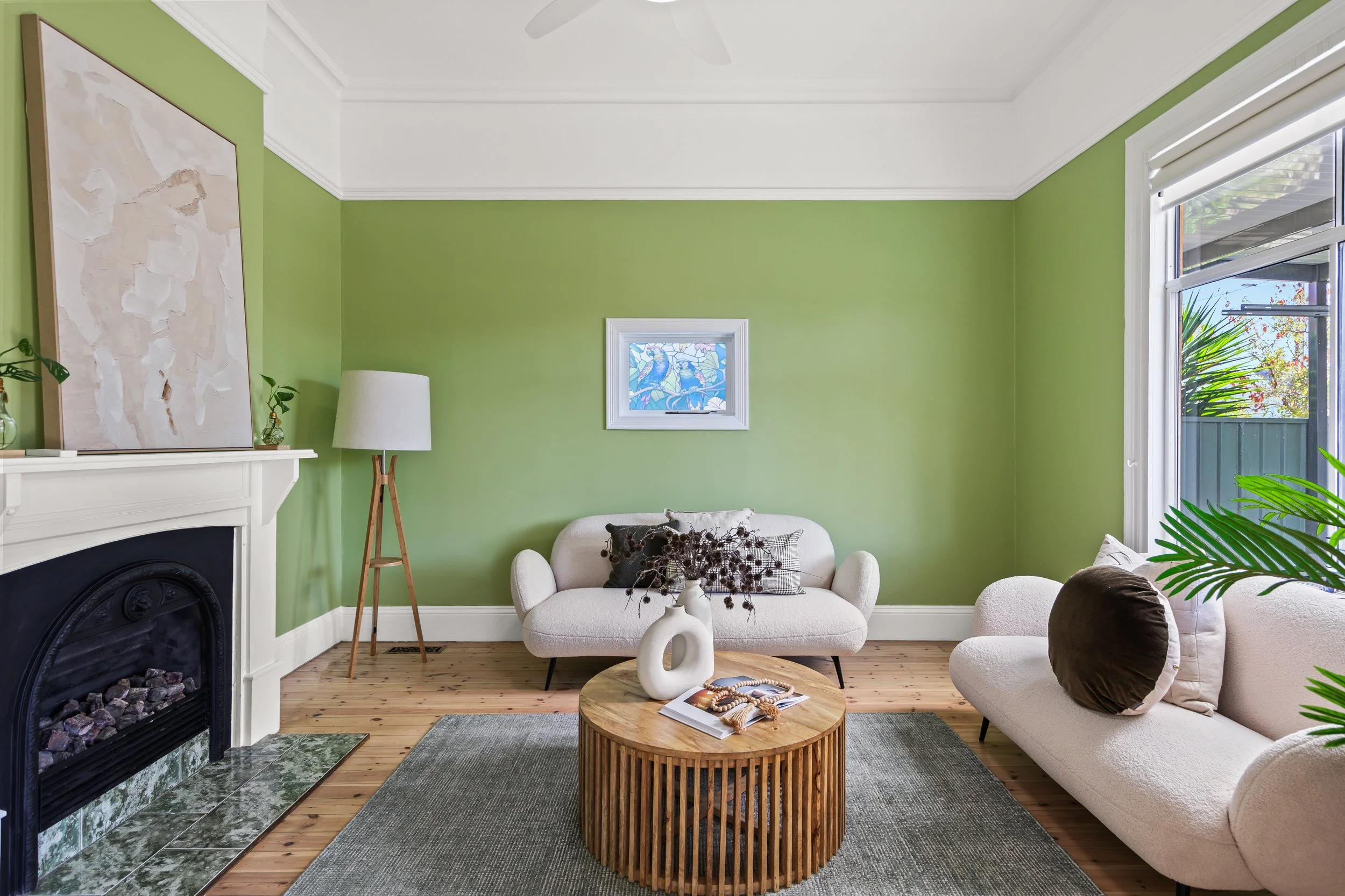 Living room with green walls, white sofas, a wooden coffee table, artwork, a fireplace, and large windows with blinds.