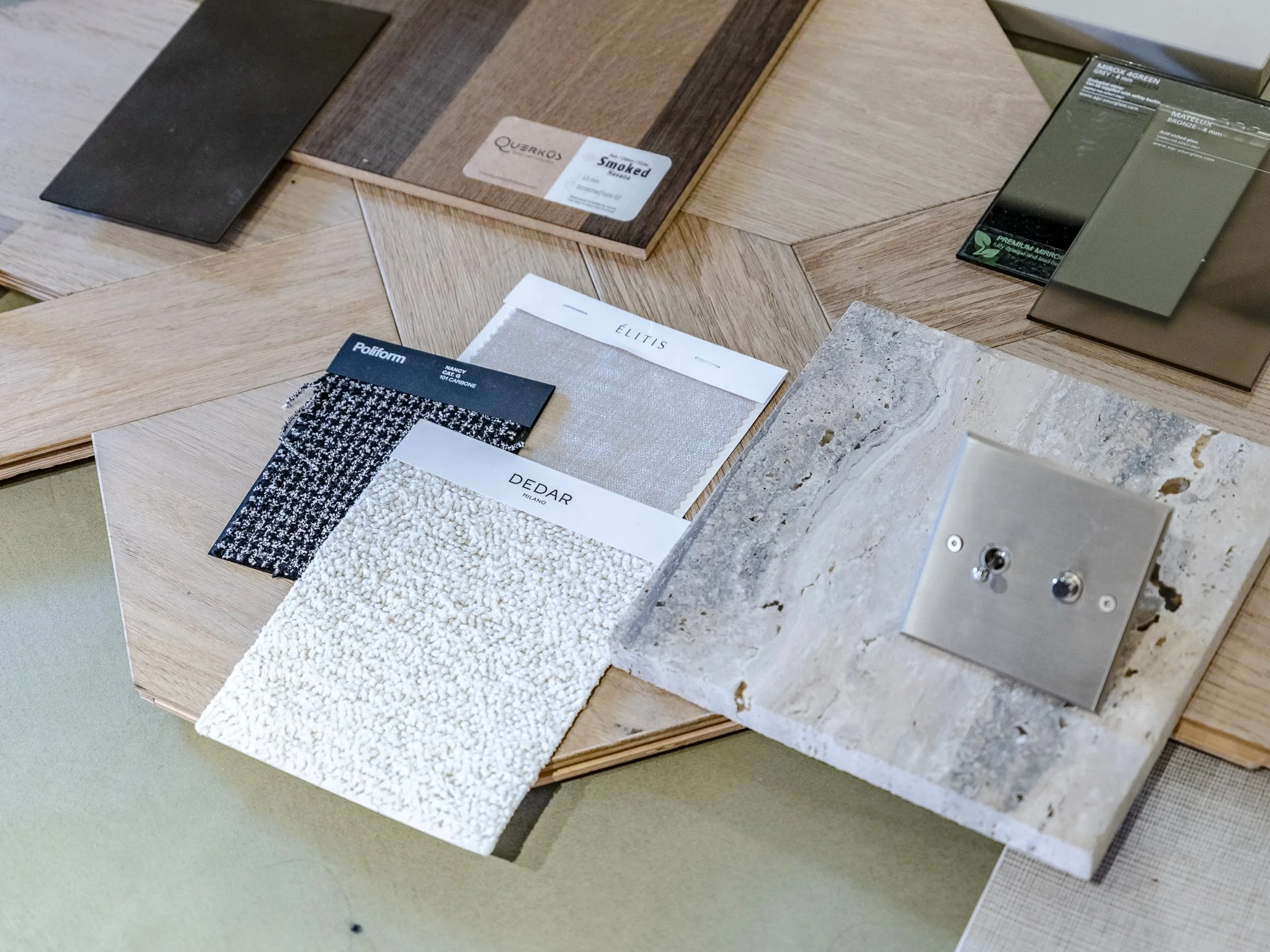 Échantillons de matériaux pour décoration intérieure, comprenant des tissus, des carrelages, des miroirs et des palettes de couleurs, exposés sur une table en bois