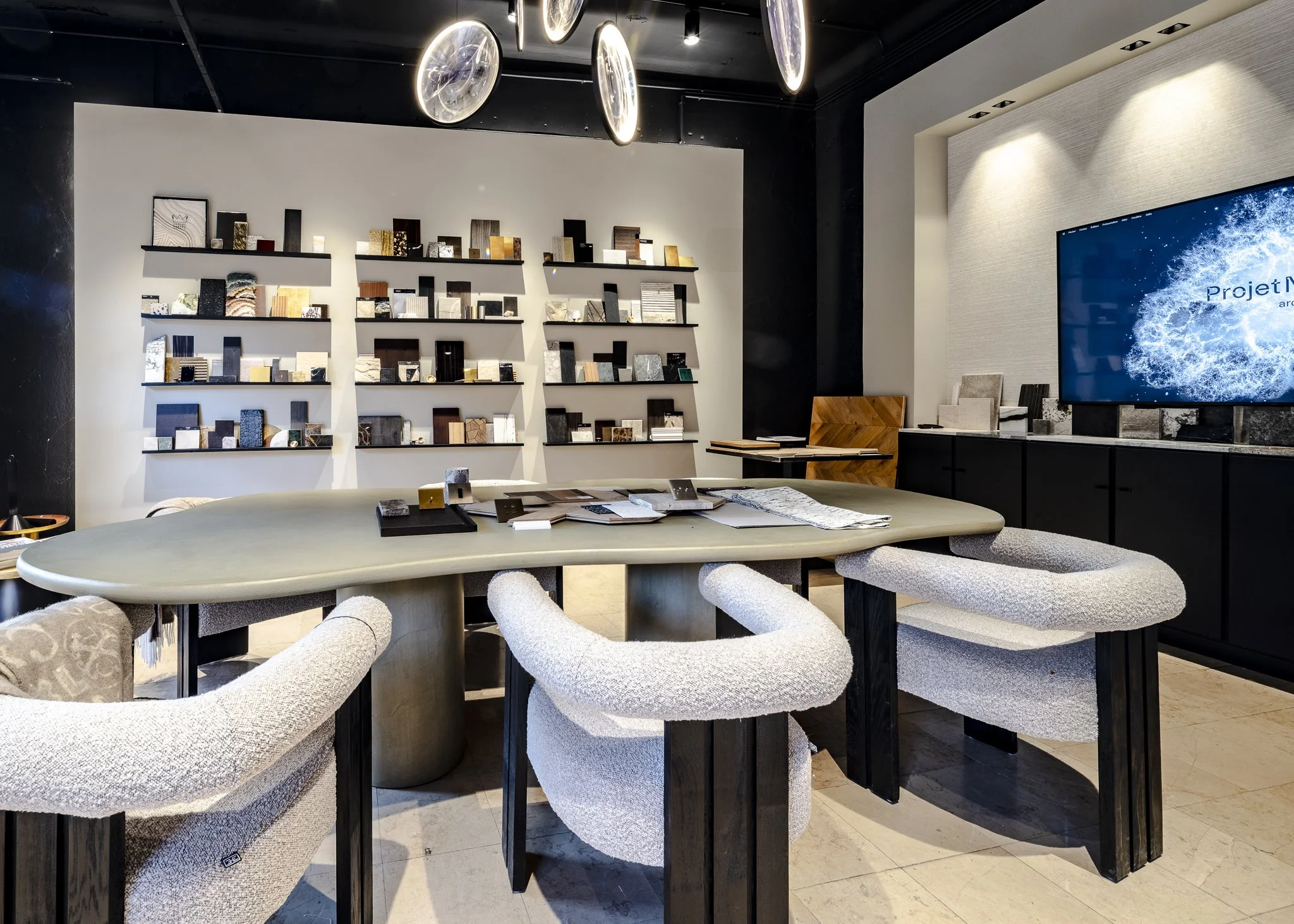 Salle de réunion moderne avec un grand tapis de conférence, des fauteuils blancs, une table ovale, des échantillons de matériaux sur la table, un mur avec des étagères de présentation de matériaux, un grand écran à écran plat sur le mur, décor contem