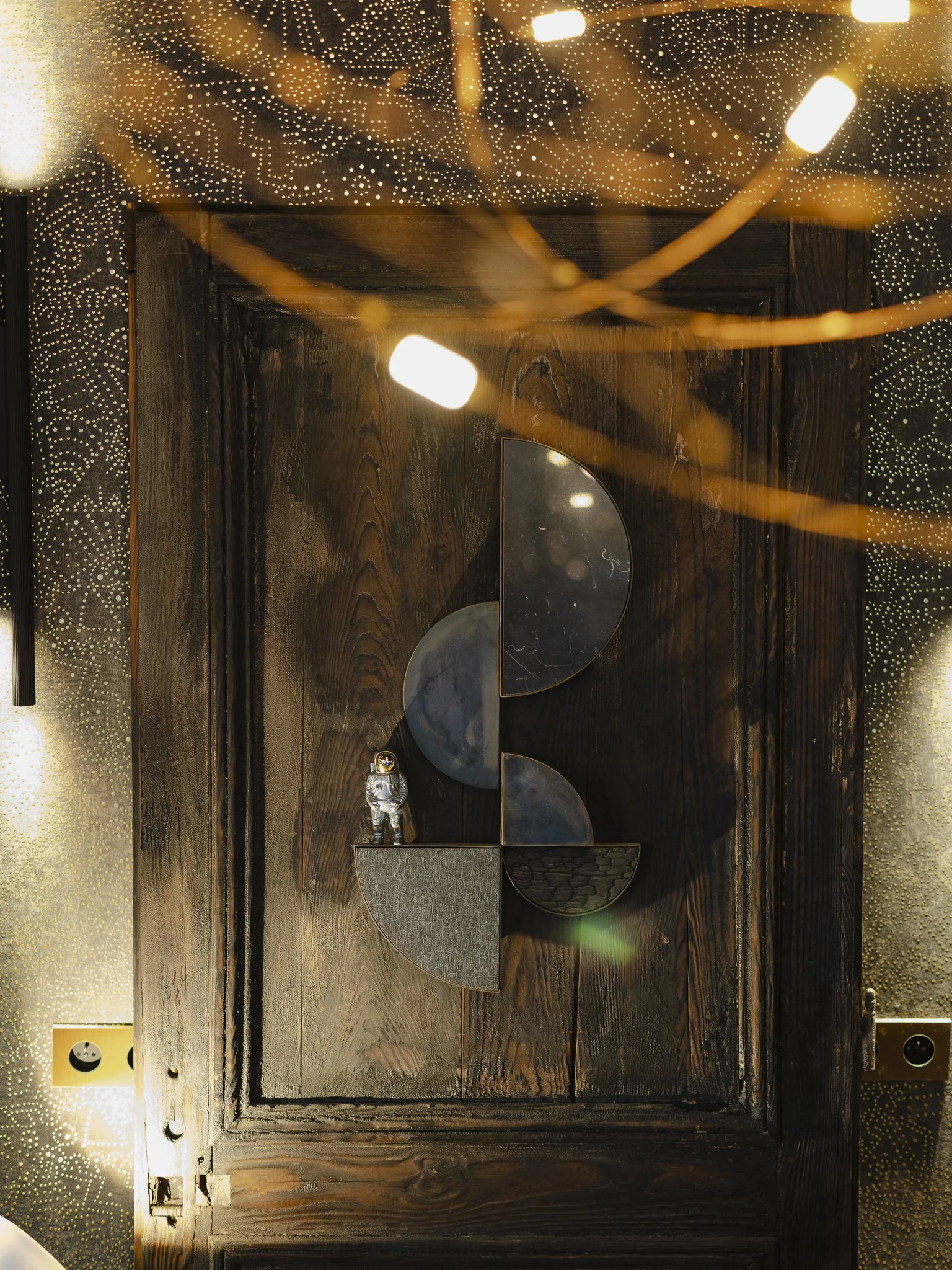 Décor mural en bois avec plusieurs pièces métalliques semi-circulaires et un petit astronaute en statue, éclairé par une lumière chaude et entouré d'une décoration scintillante.