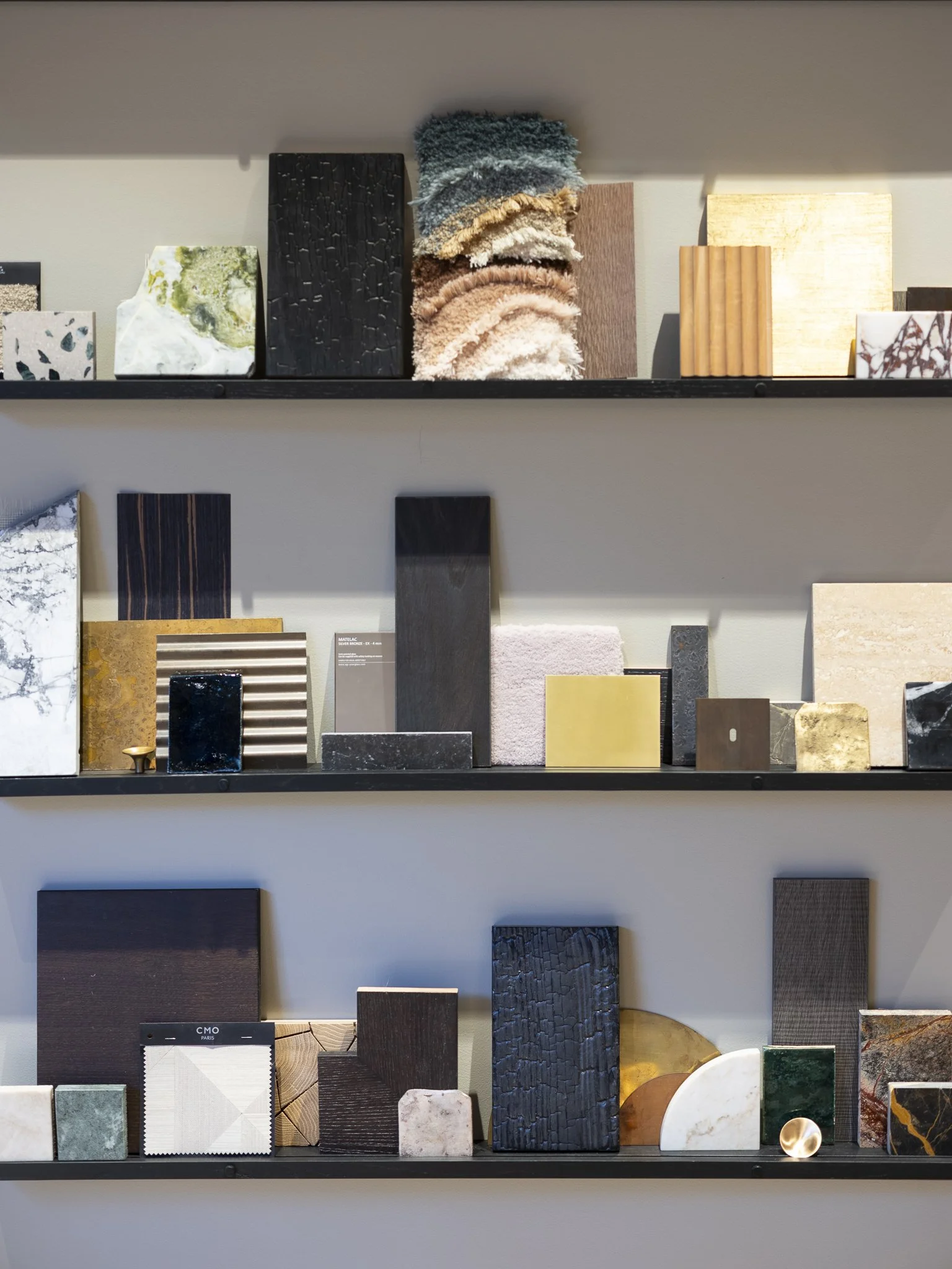 Étagères avec divers échantillons de matériaux de surface, y compris bois, pierre, marbre, céramique, et textiles pour décoration intérieure.