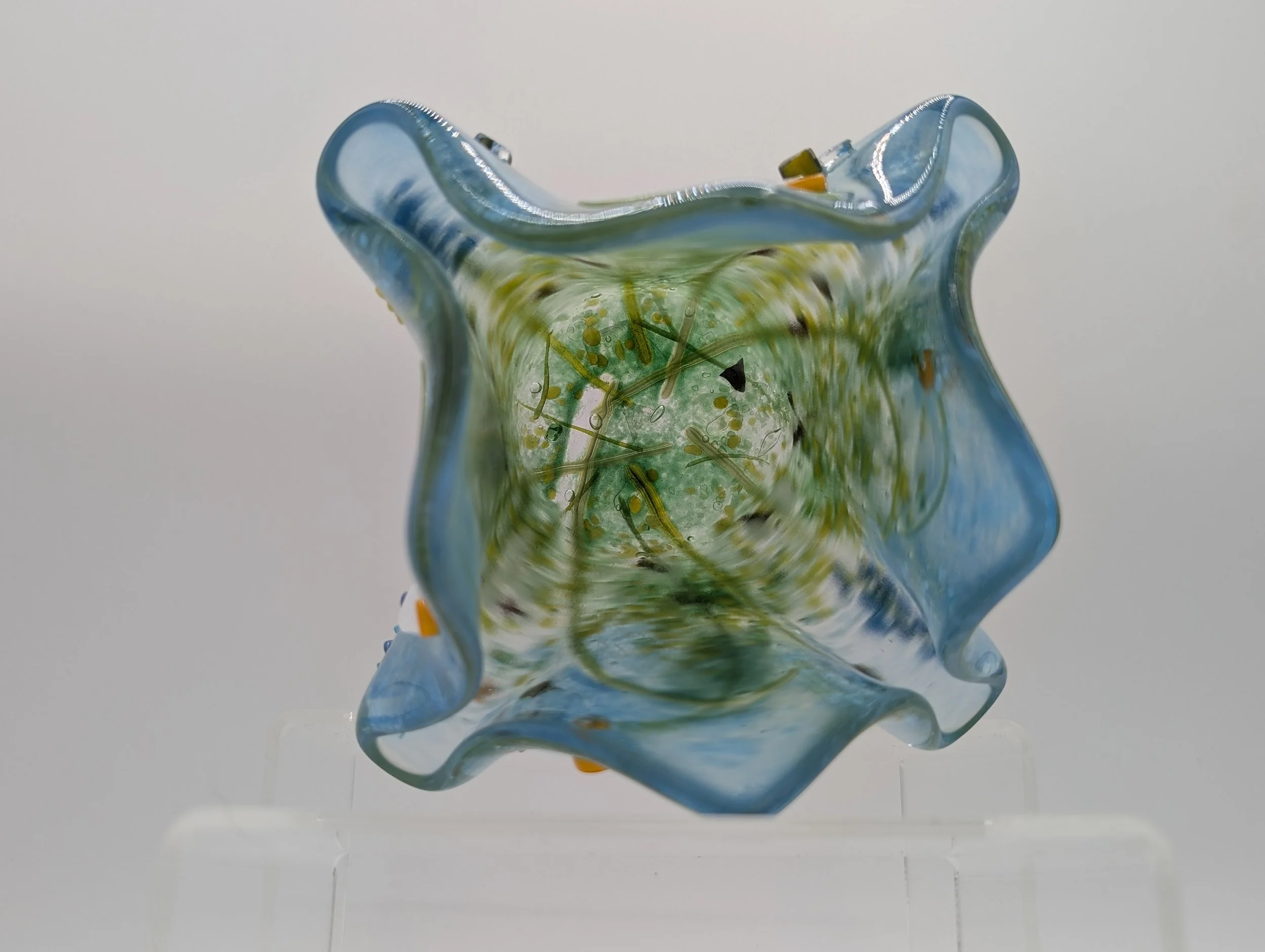 Top-down view into Meadow Dew's icy blue wavy rim and swirling green frit interior, on a clear stand